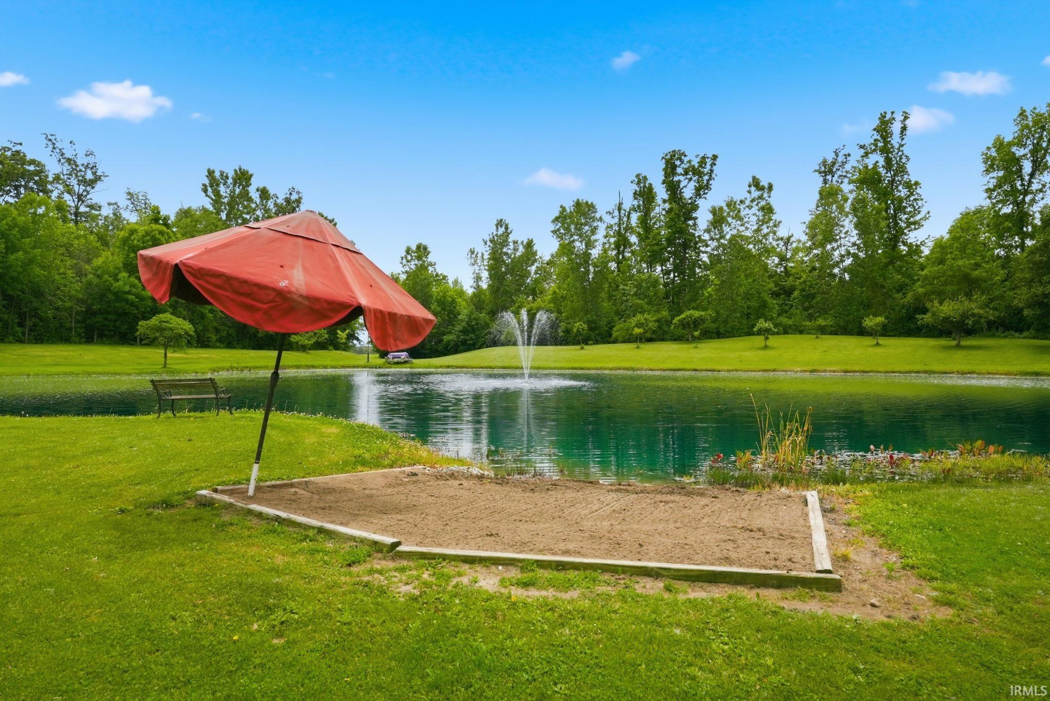 Expansive pond featuring a central fountain, surrounded by lush green lawns and mature trees