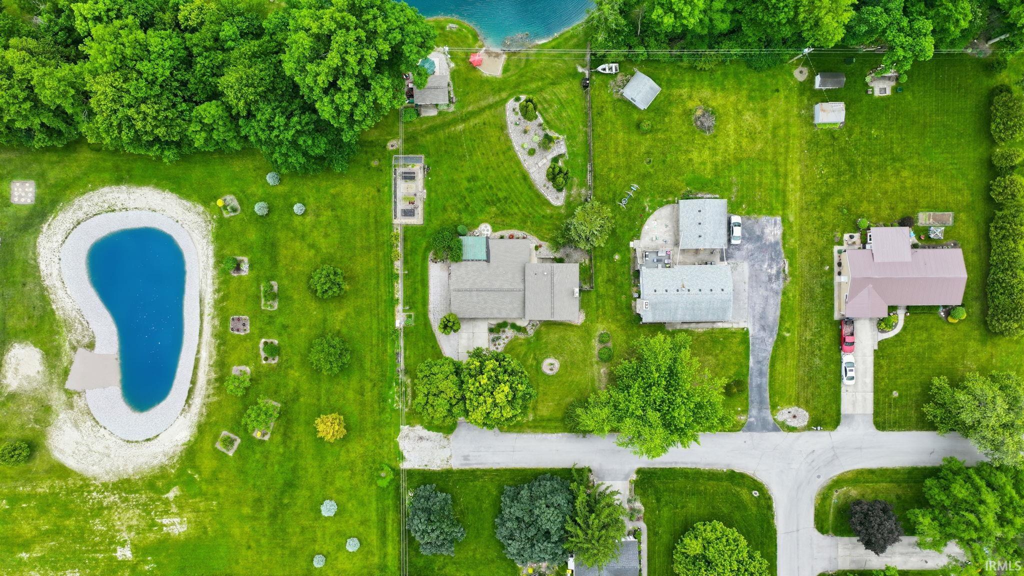 Expansive property featuring a prominent irregularly shaped pond with a surrounding sandy edge, a manicured green lawn, mature trees, and multiple outbuildings
