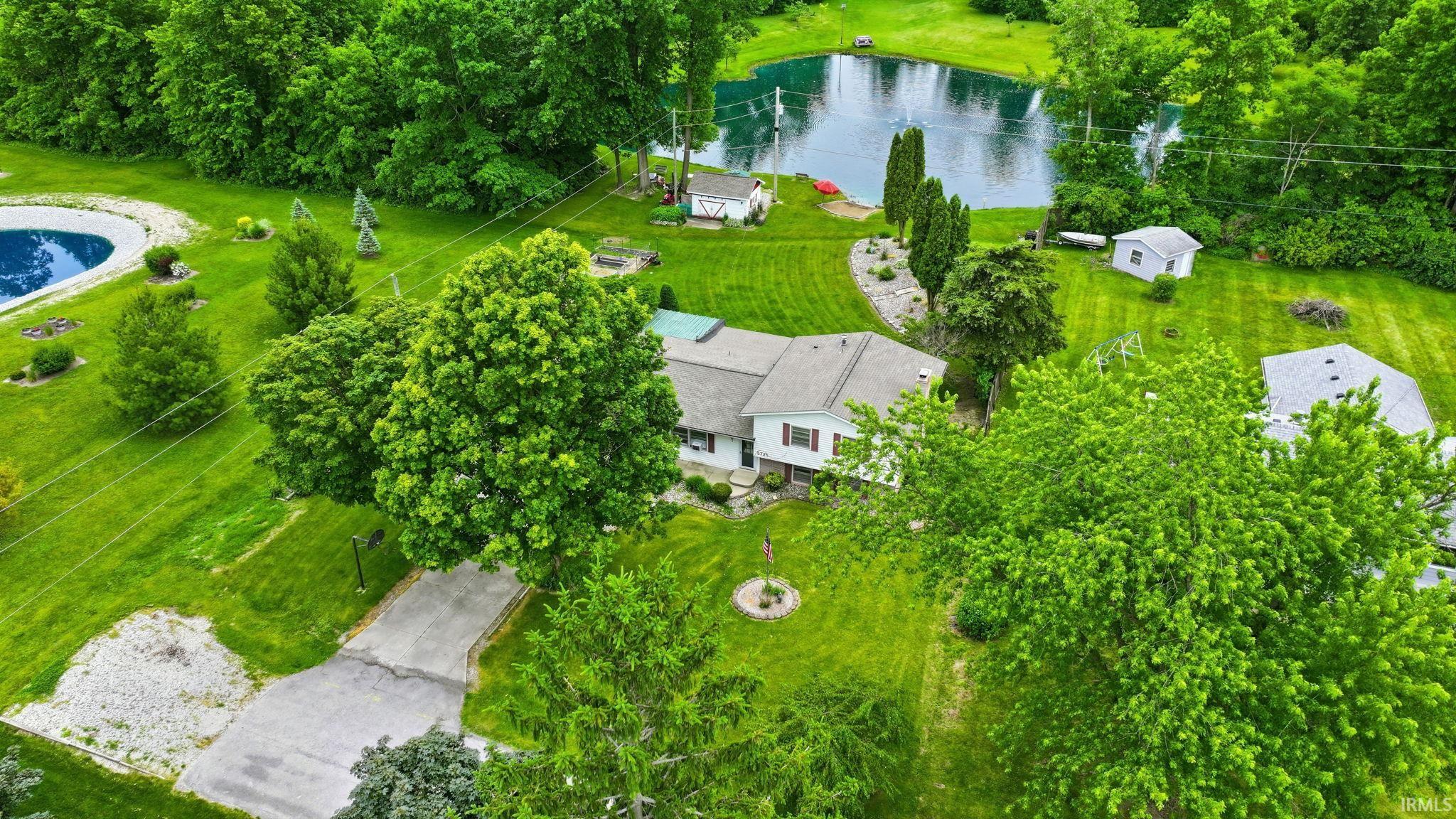 Expansive property featuring a private pond, mature trees, a well-maintained lawn, and a paved driveway