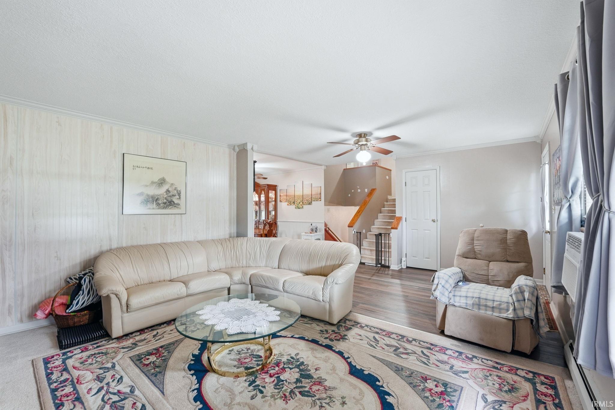 Bright living area featuring wood-finish flooring, a ceiling fan with integrated lighting, and a white paneled accent wall