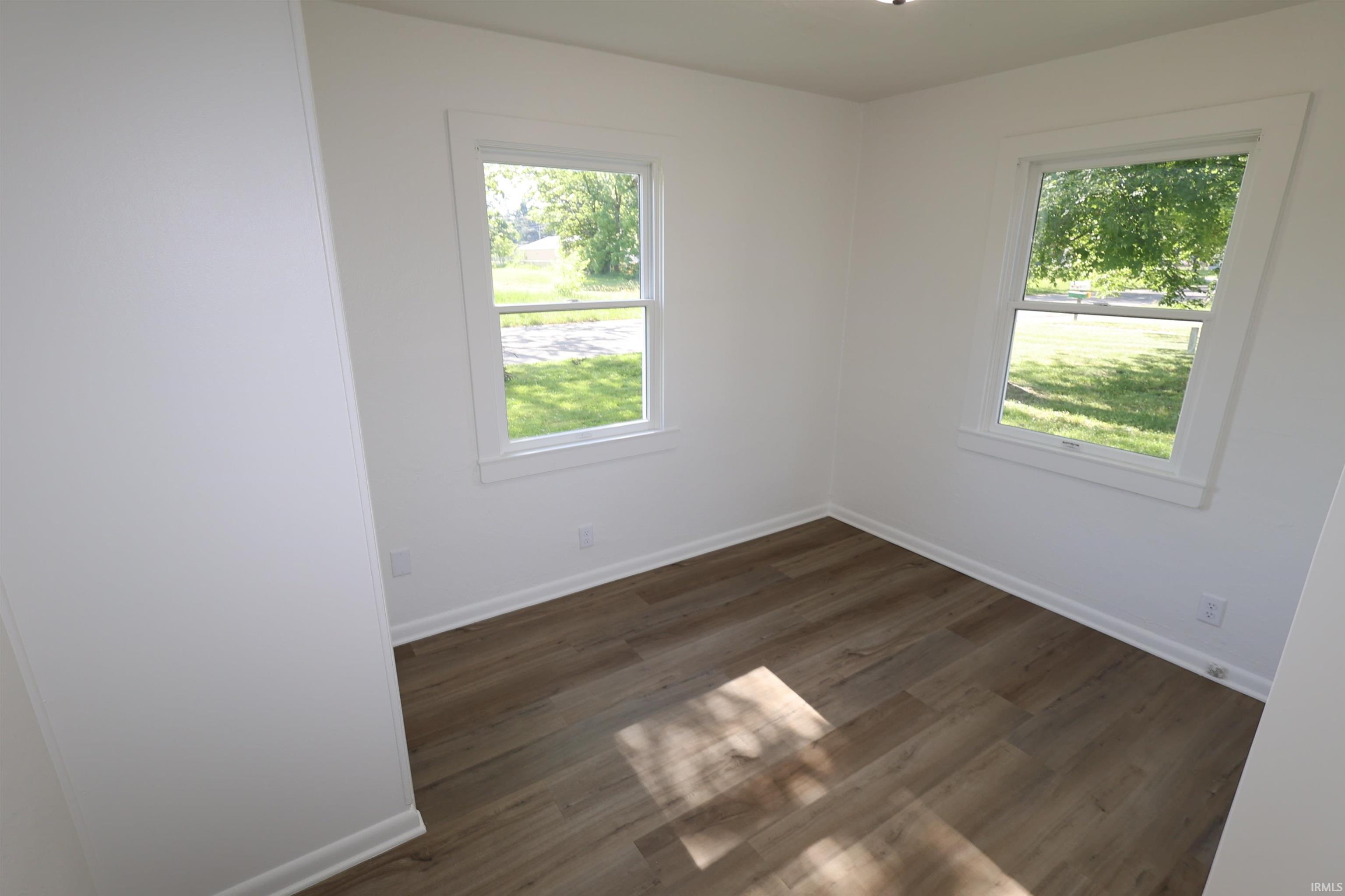Room featuring wood-finish flooring, two sash windows with white trim, and white painted walls