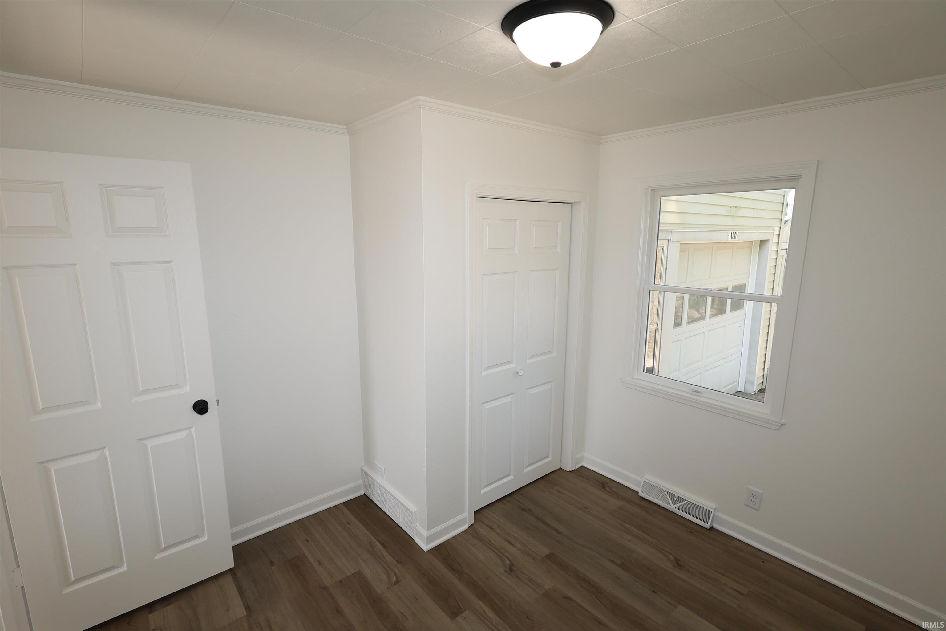 Room featuring wood-finish flooring, crisp white walls, a six-panel door with black hardware, a bi-fold closet door, and a single window with white trim