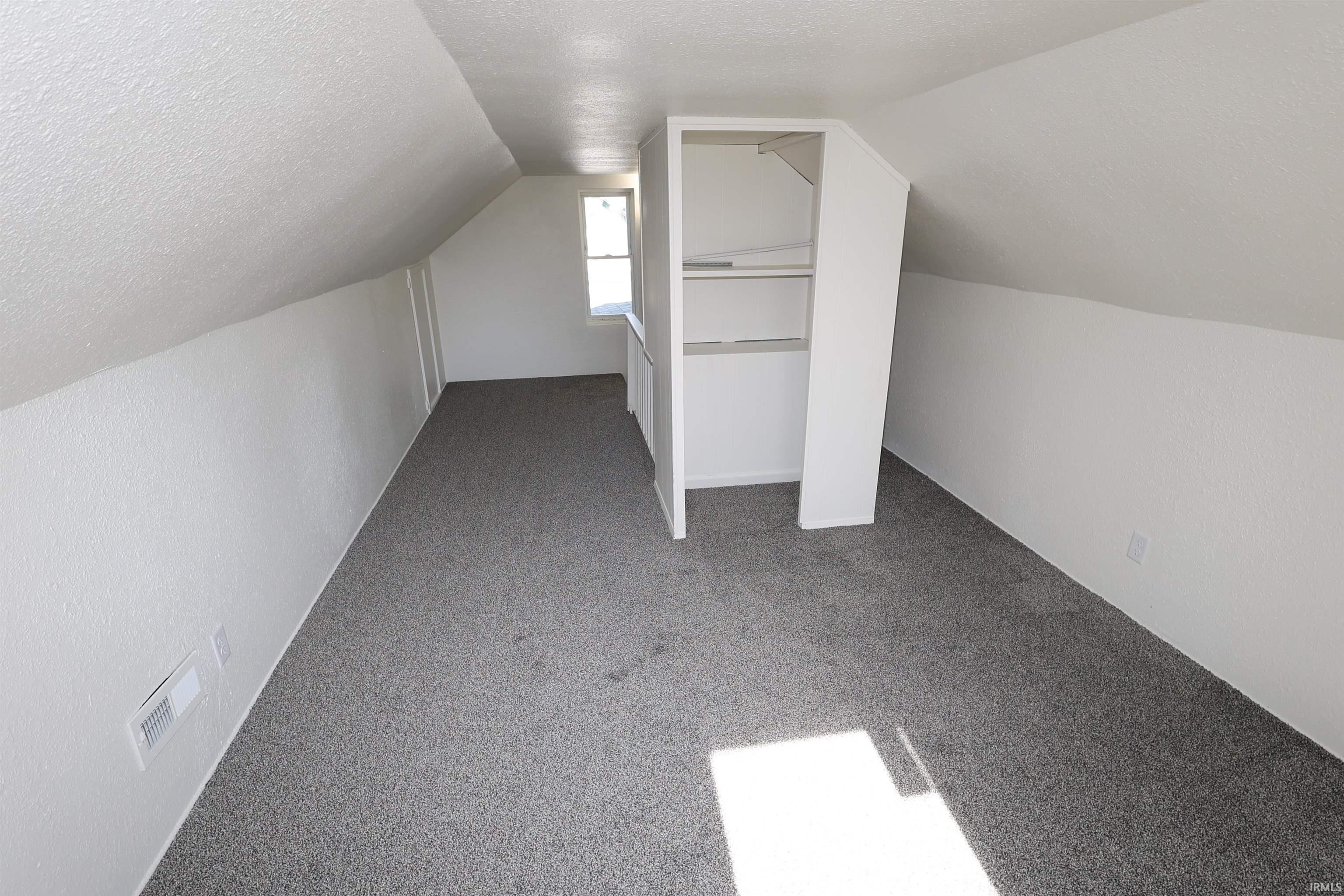 Room featuring gray textured carpeting, white painted walls with a textured finish, sloped ceilings, a single window, and a built-in closet with shelving