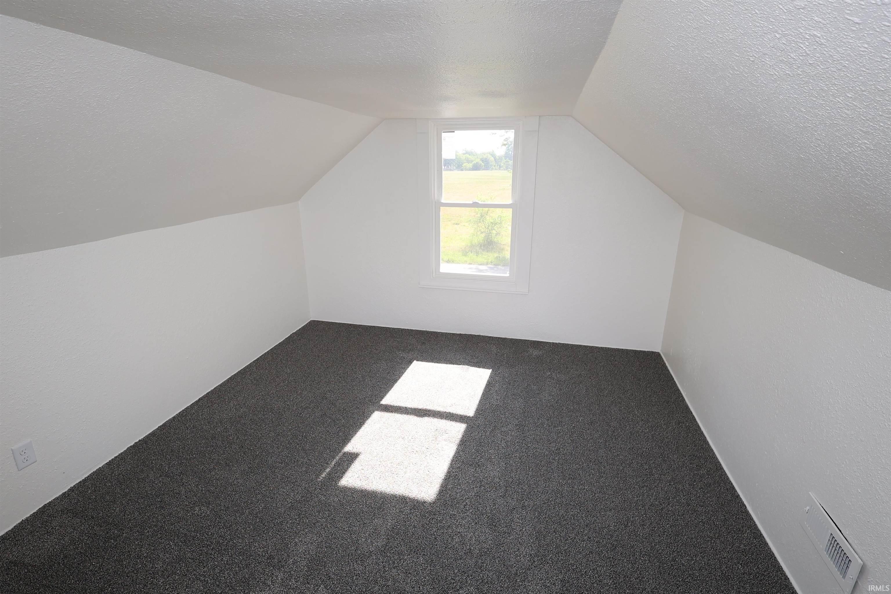 Sloped ceiling room featuring a single window, dark gray carpet, white walls, and a wall-mounted vent