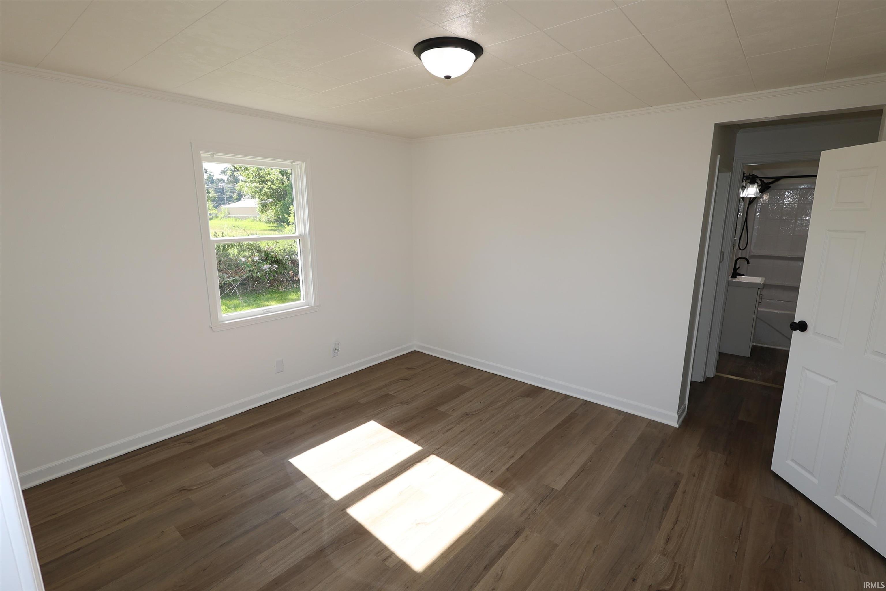 Wood-finish flooring with white baseboards, a white-framed window, and a flush mount ceiling light