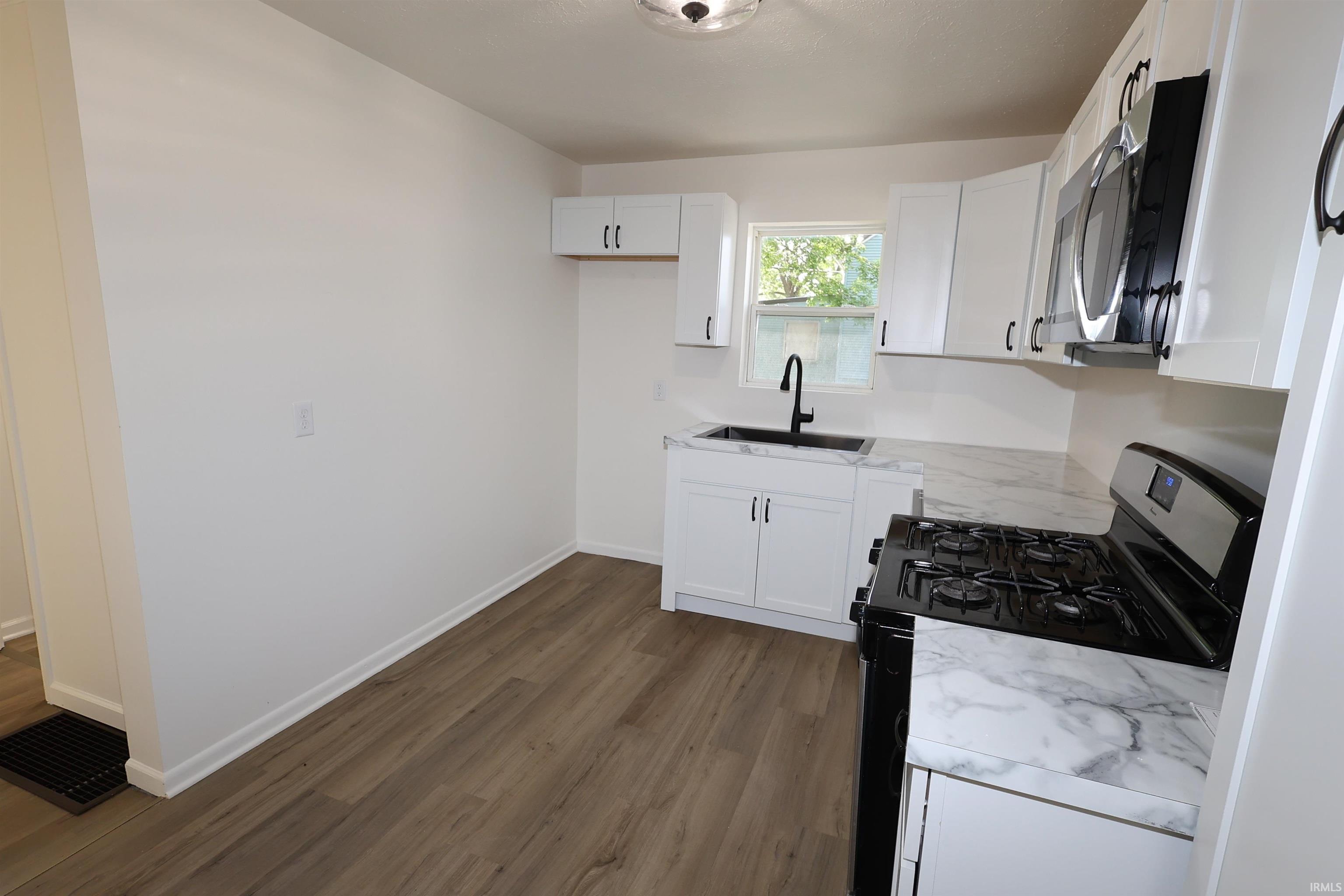 Kitchen featuring white cabinetry, marbled countertops, and wood-finish flooring