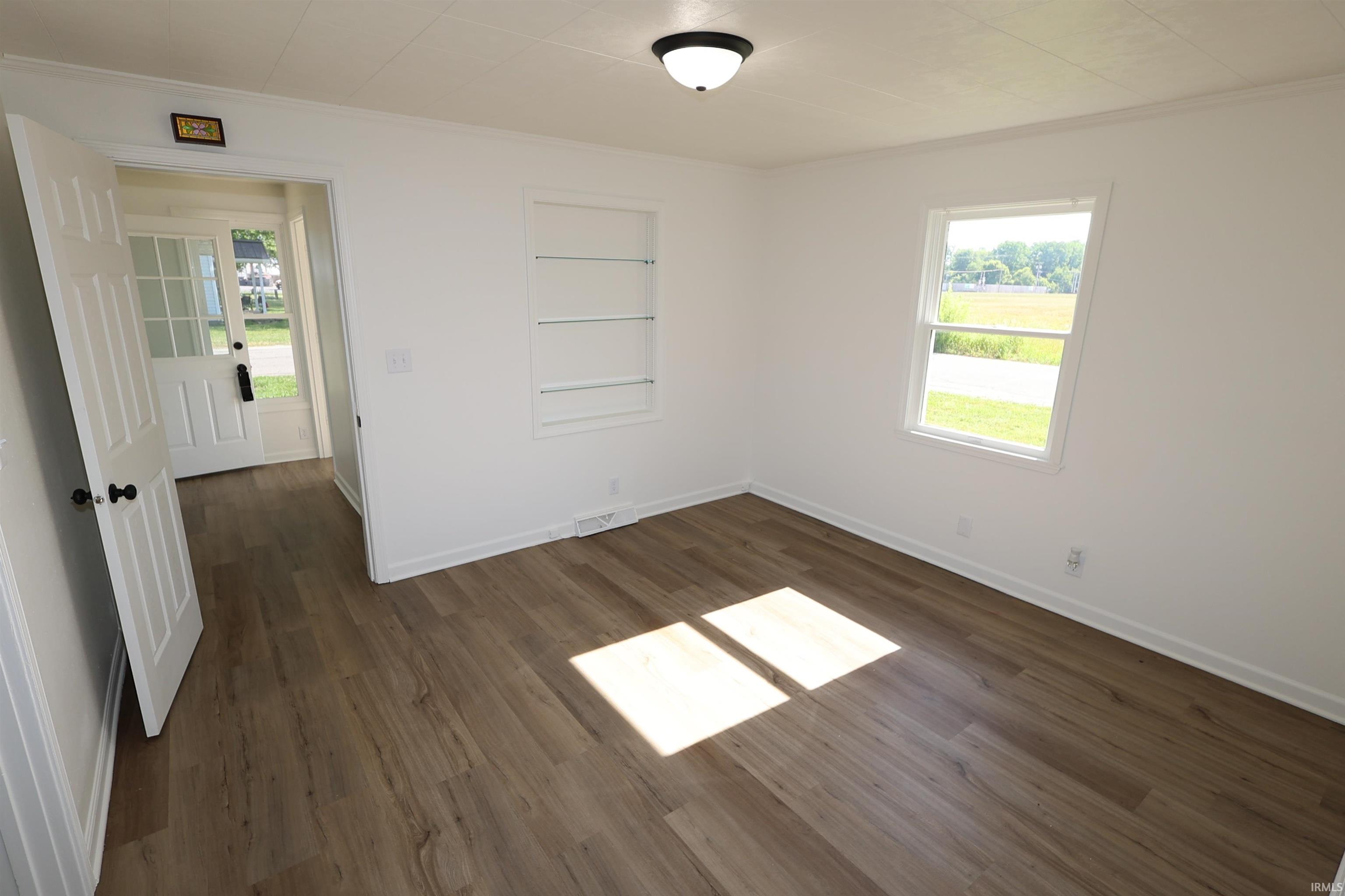 Room featuring wood-finish flooring, white walls, built-in shelving, and a paneled entry door with glass inserts