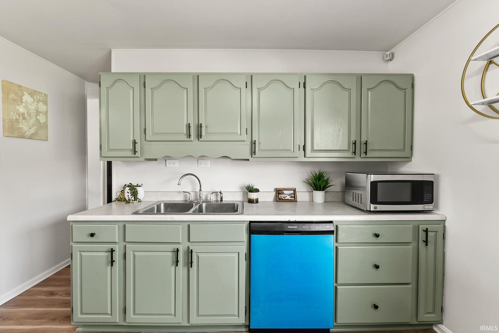 Kitchen featuring sage green cabinetry with black hardware, white countertops, a double basin stainless steel sink with gooseneck faucet, and wood-finish flooring