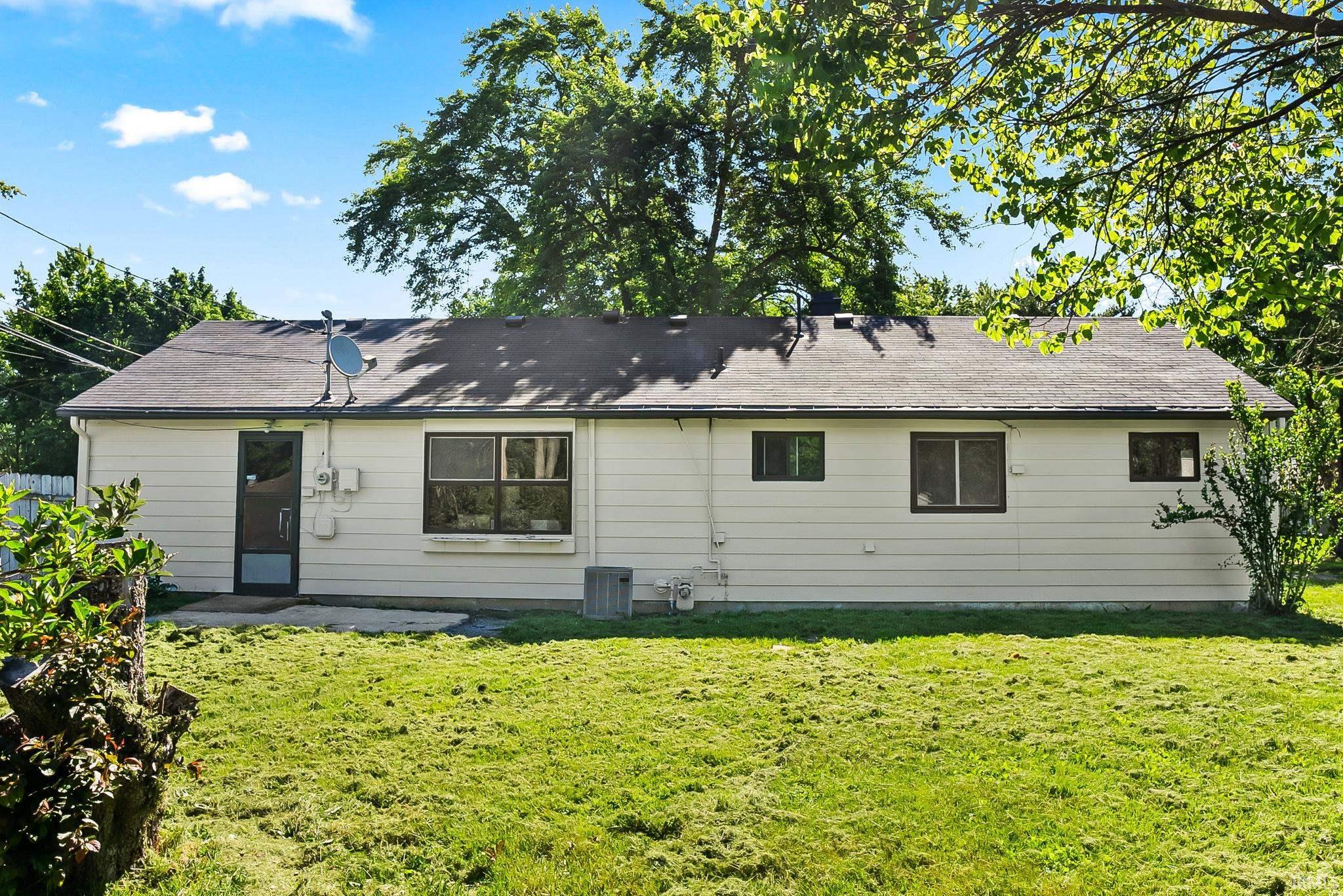 Rear exterior featuring white horizontal siding, a dark asphalt shingle roof, and multiple windows with dark frames