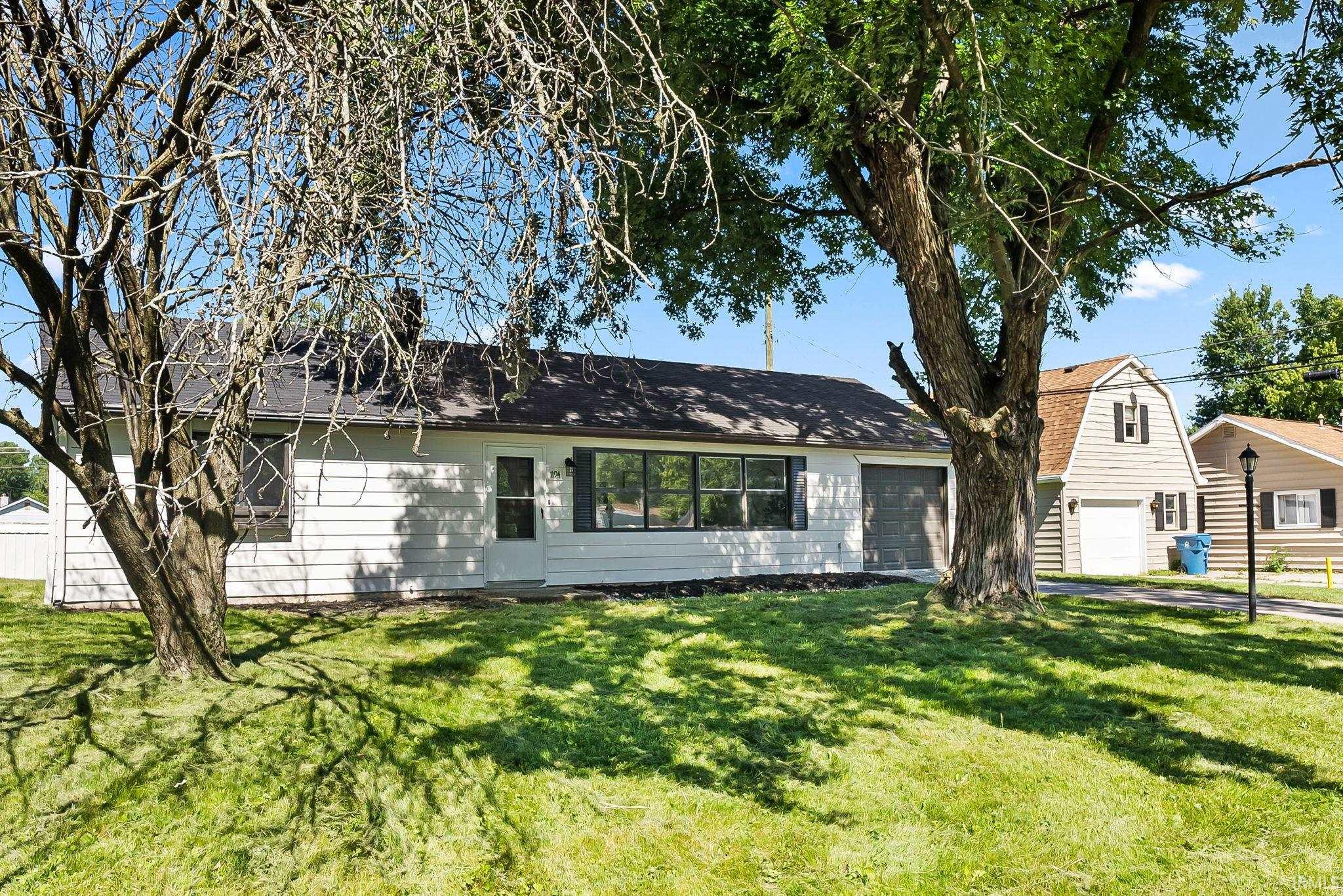 Ranch-style exterior featuring white siding, a dark shingle roof, and an attached garage with a dark gray door
