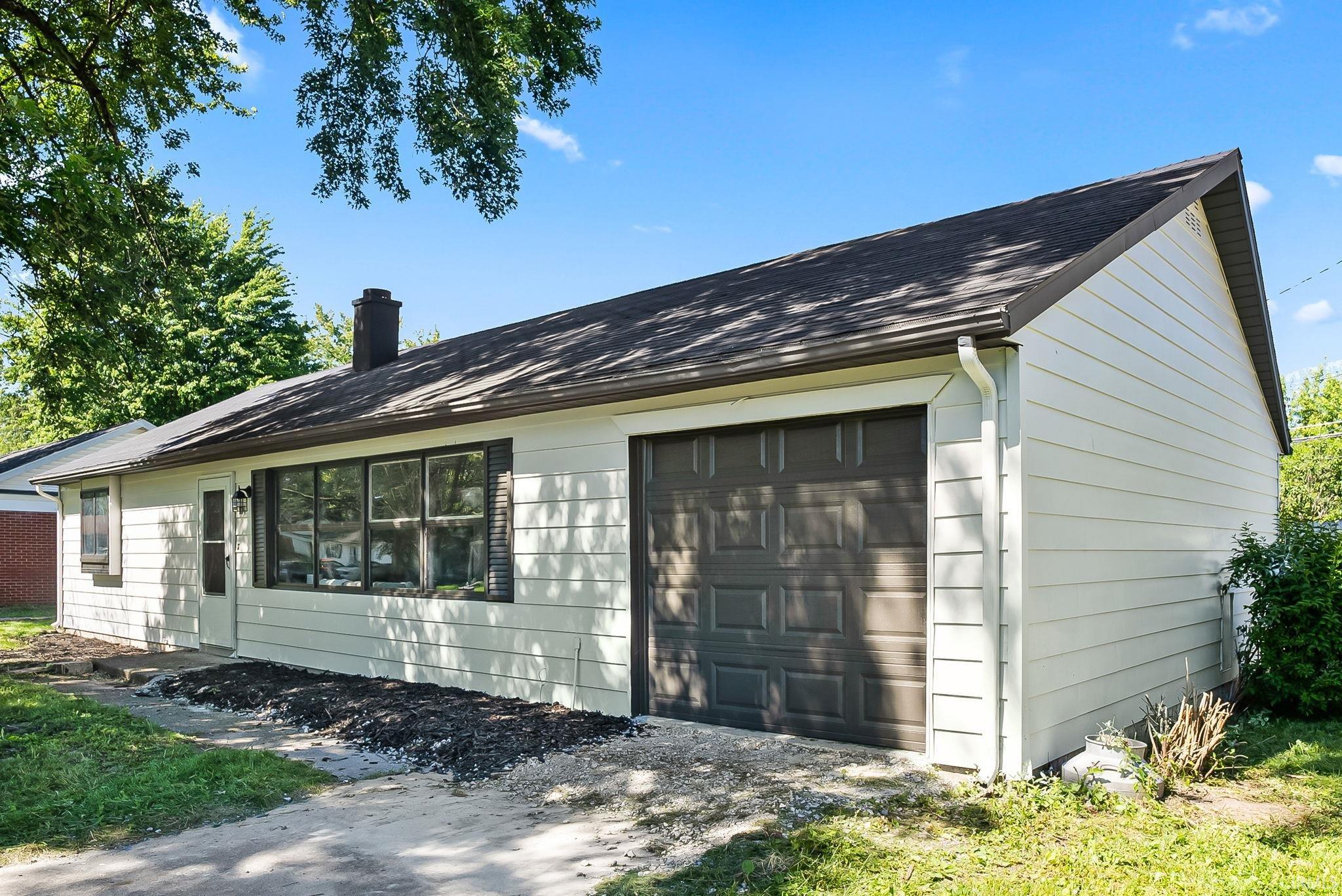 Single-story residence featuring light-colored siding, a dark asphalt shingle roof, and an attached garage with a panel door