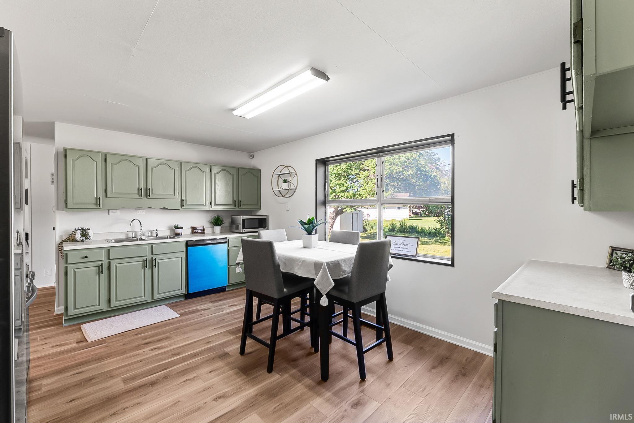 Kitchen featuring wood-finish flooring, light green cabinetry with dark hardware, a white countertop, and a double-basin sink