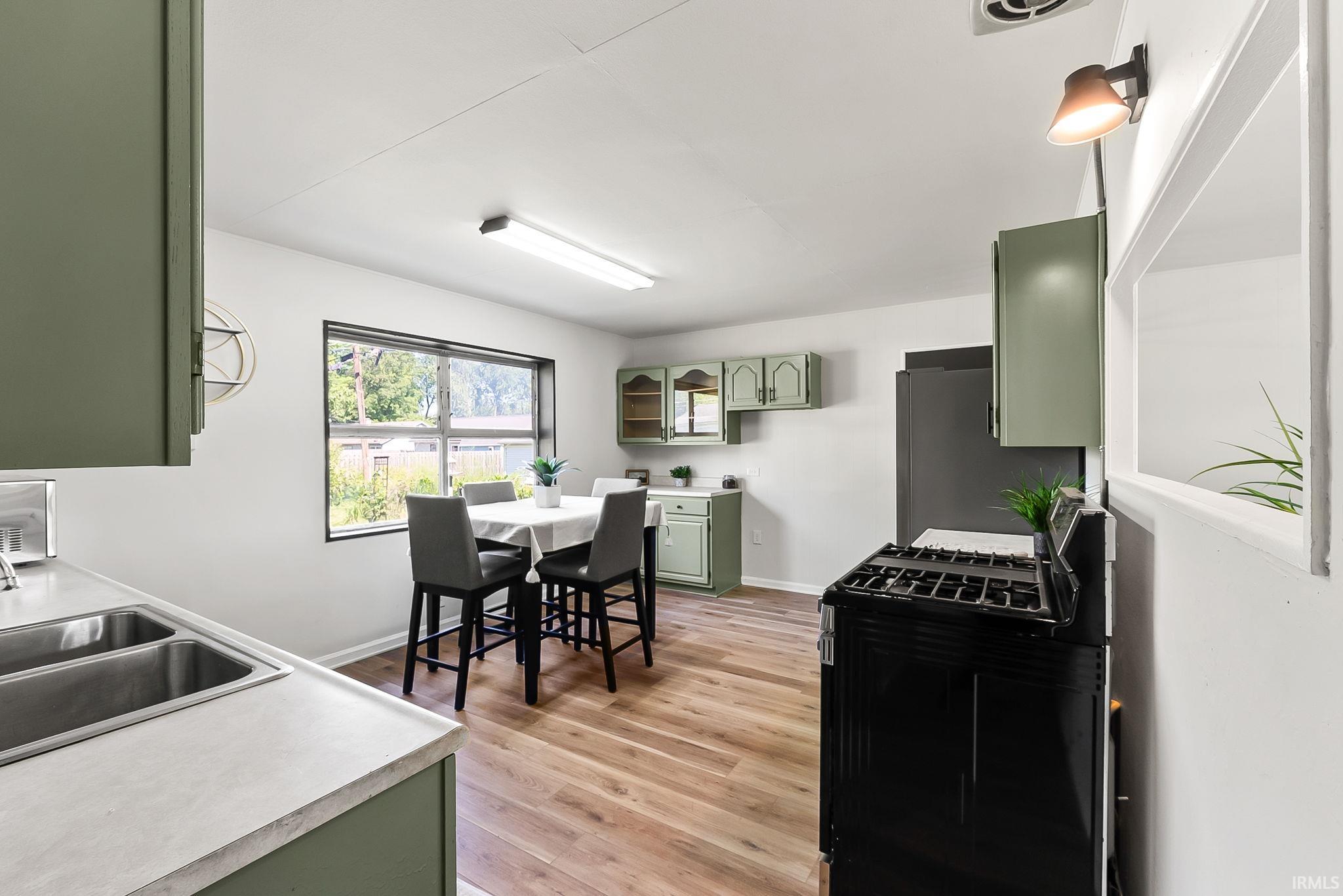 Kitchen featuring wood-finish flooring, sage green cabinetry, a double basin sink, and a black range