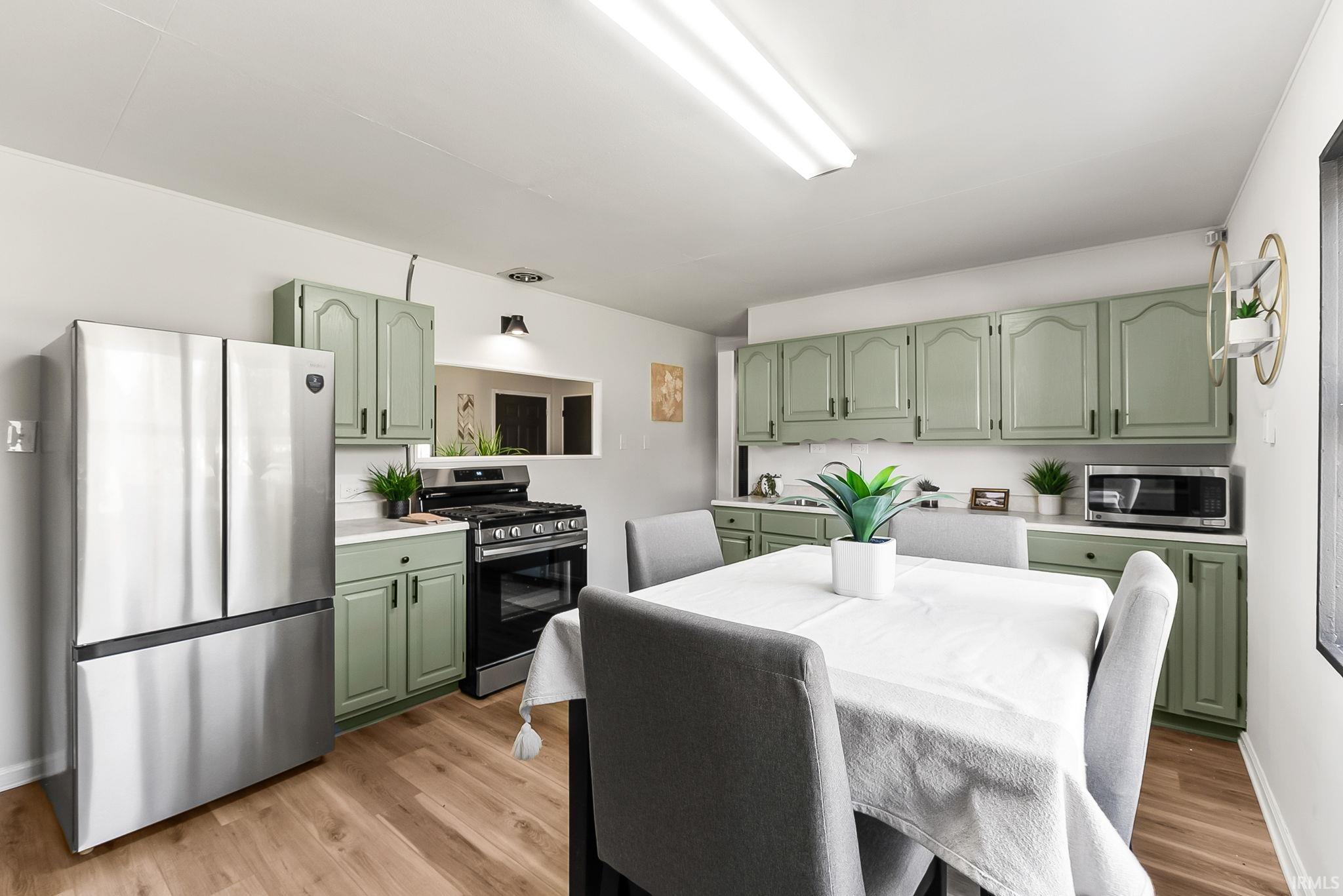 Kitchen featuring light green cabinetry, stainless steel appliances, wood-finish flooring, white countertops, and a pass-through window