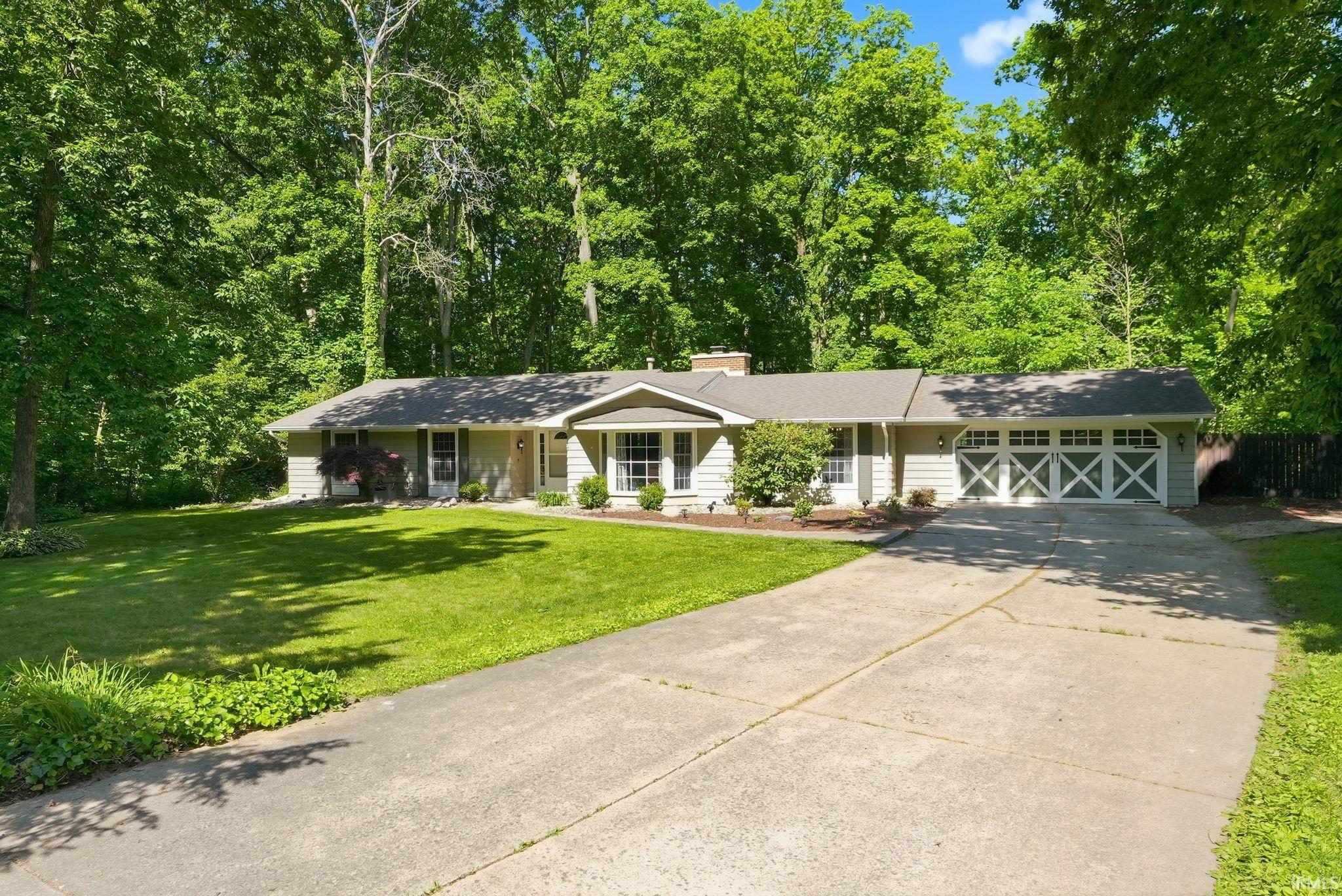 Ranch-style residence featuring light-colored siding, a dark shingle roof, and a prominent two-car garage with cross-brace details