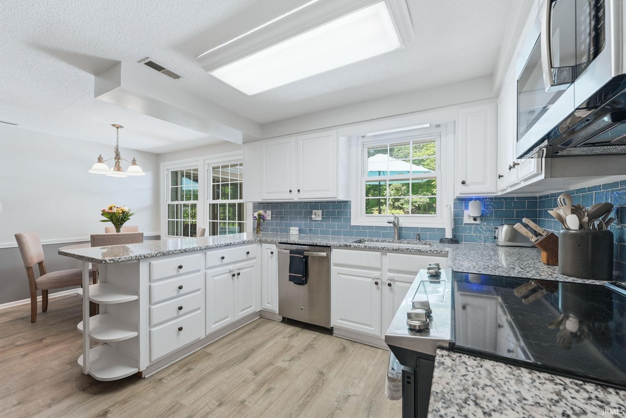 Kitchen featuring granite countertops, white cabinetry with black hardware, a blue subway tile backsplash, and stainless steel appliances