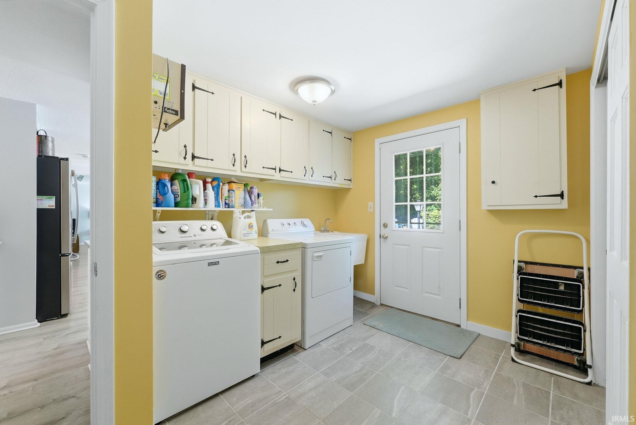 Dedicated utility room featuring extensive upper cabinetry, a single-pane glass exterior door, light-toned flooring, countertop workspace, and a utility sink