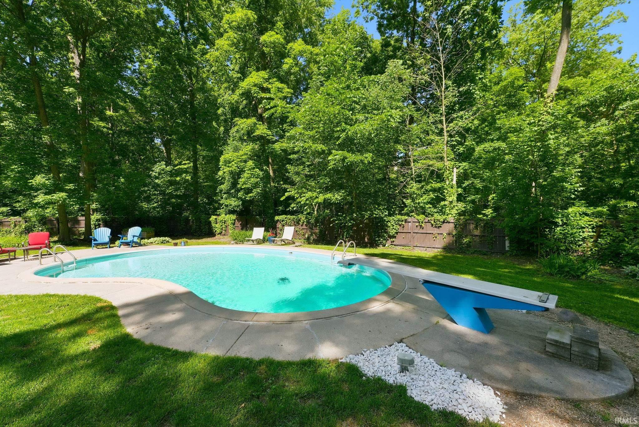 Curved swimming pool with a concrete surround, diving board, and integrated steps