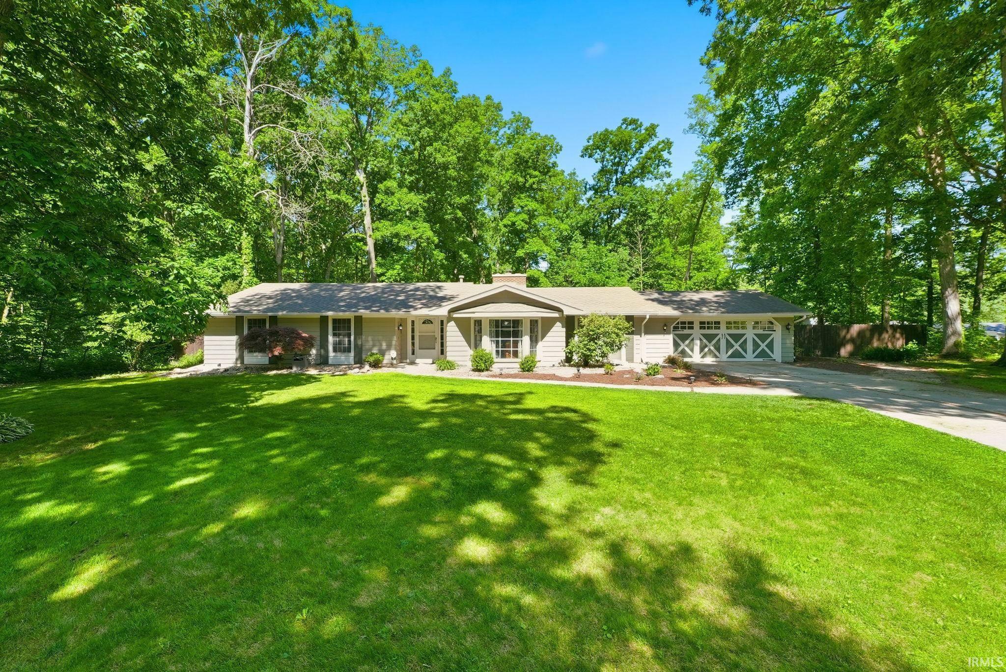 Ranch-style residence featuring a light-toned exterior siding, a prominent front lawn, a driveway, and an attached two-car garage with cross-brace doors