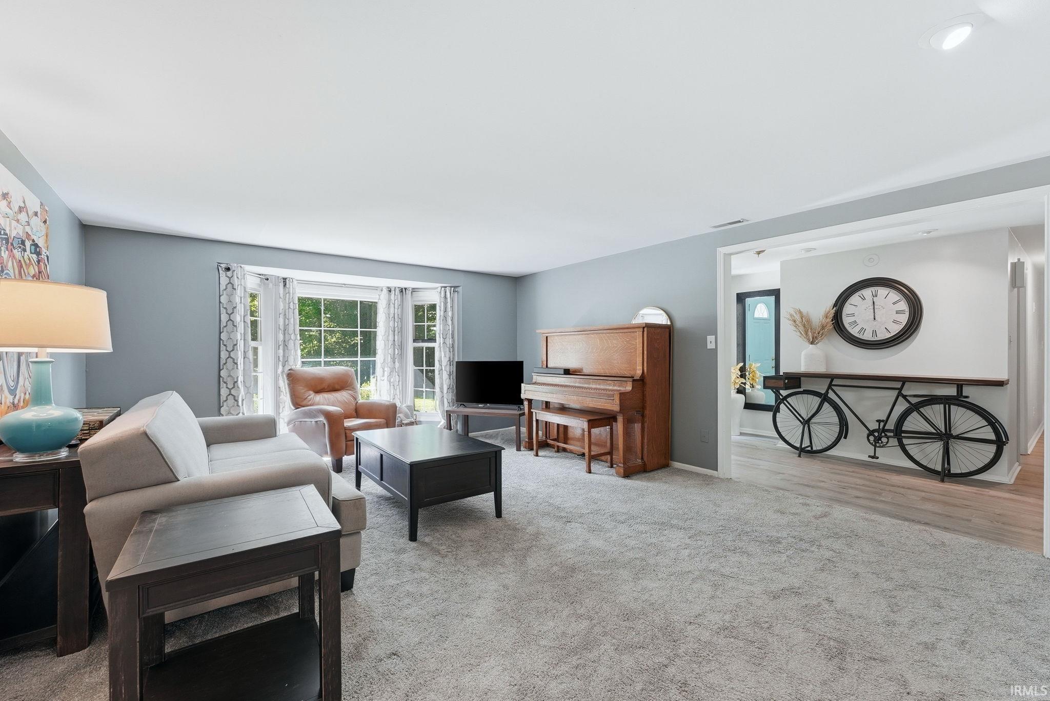 Spacious living area featuring light gray wall paint, light gray carpet flooring, and a bay window