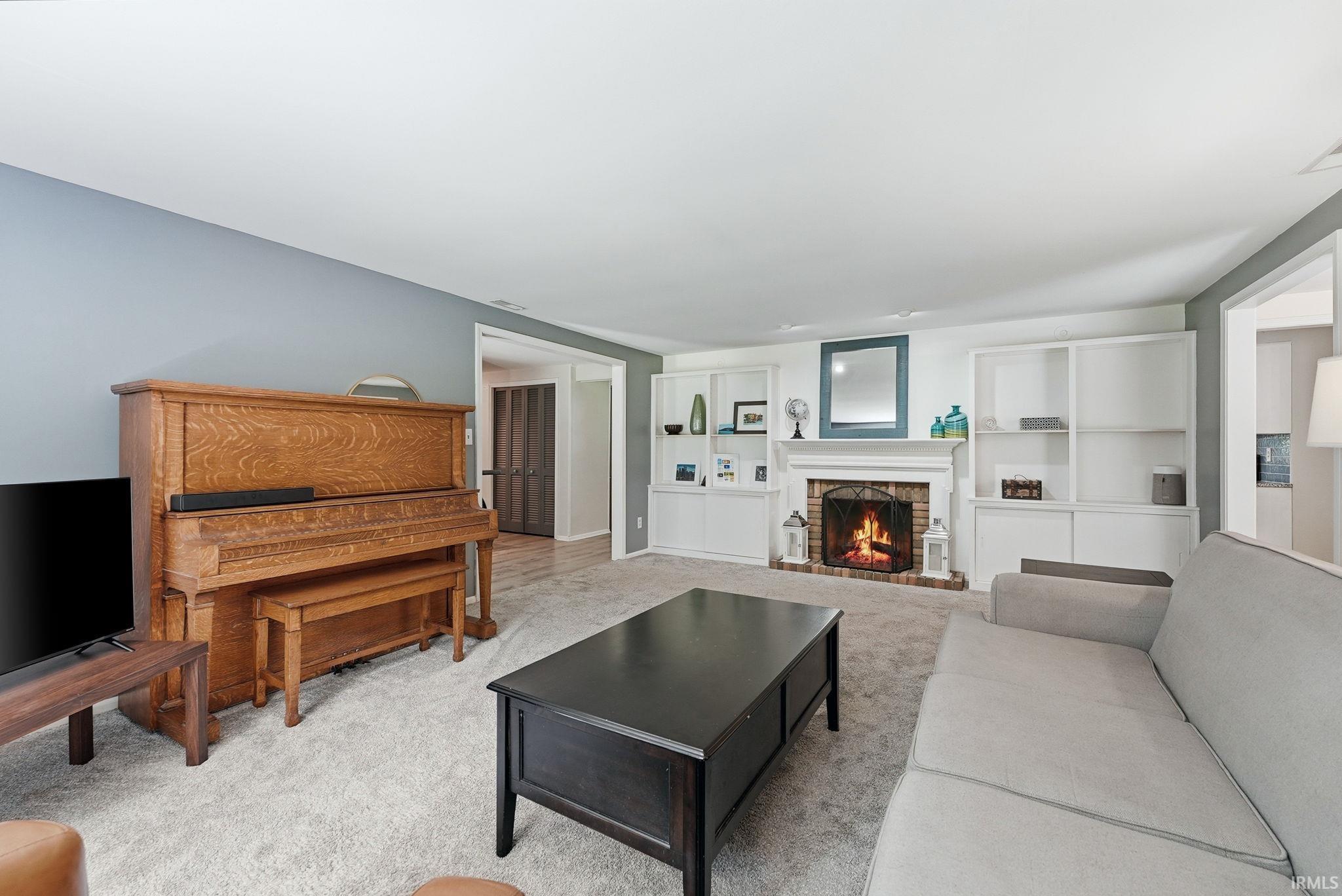 Living area featuring a brick fireplace with a white mantel, built-in shelving, light gray carpeting, and light blue wall accents