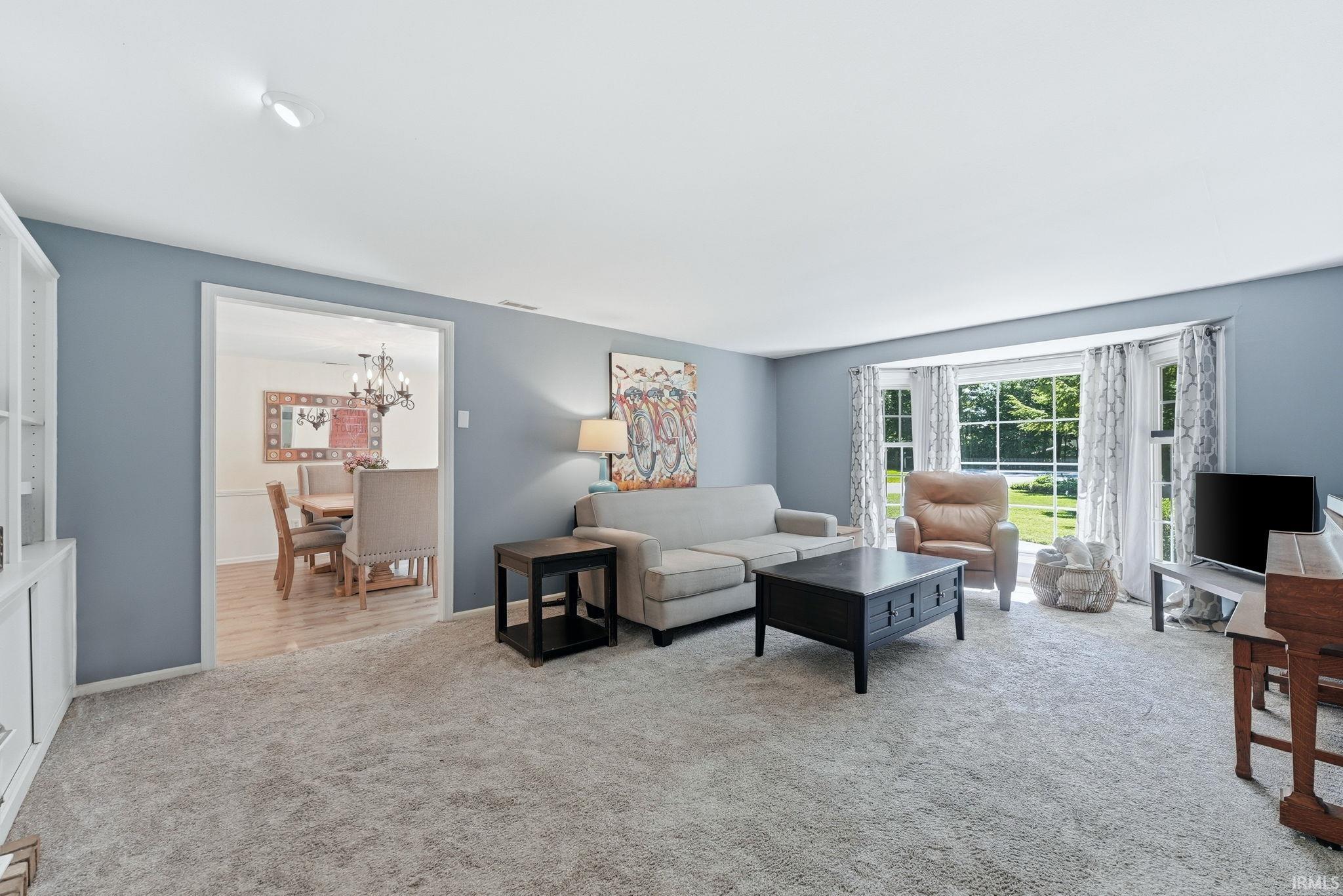 Spacious living area featuring light gray carpeting, a bay window with multiple panes, and light blue walls