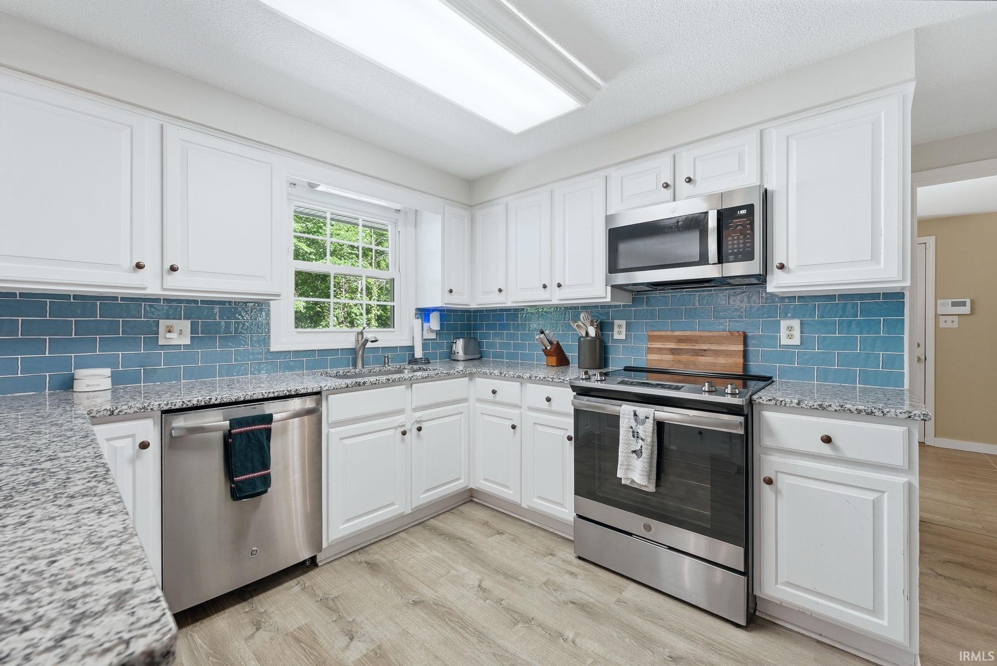 Kitchen featuring white cabinetry with dark hardware, a blue subway tile backsplash, light-toned wood-finish flooring, and stainless steel appliances