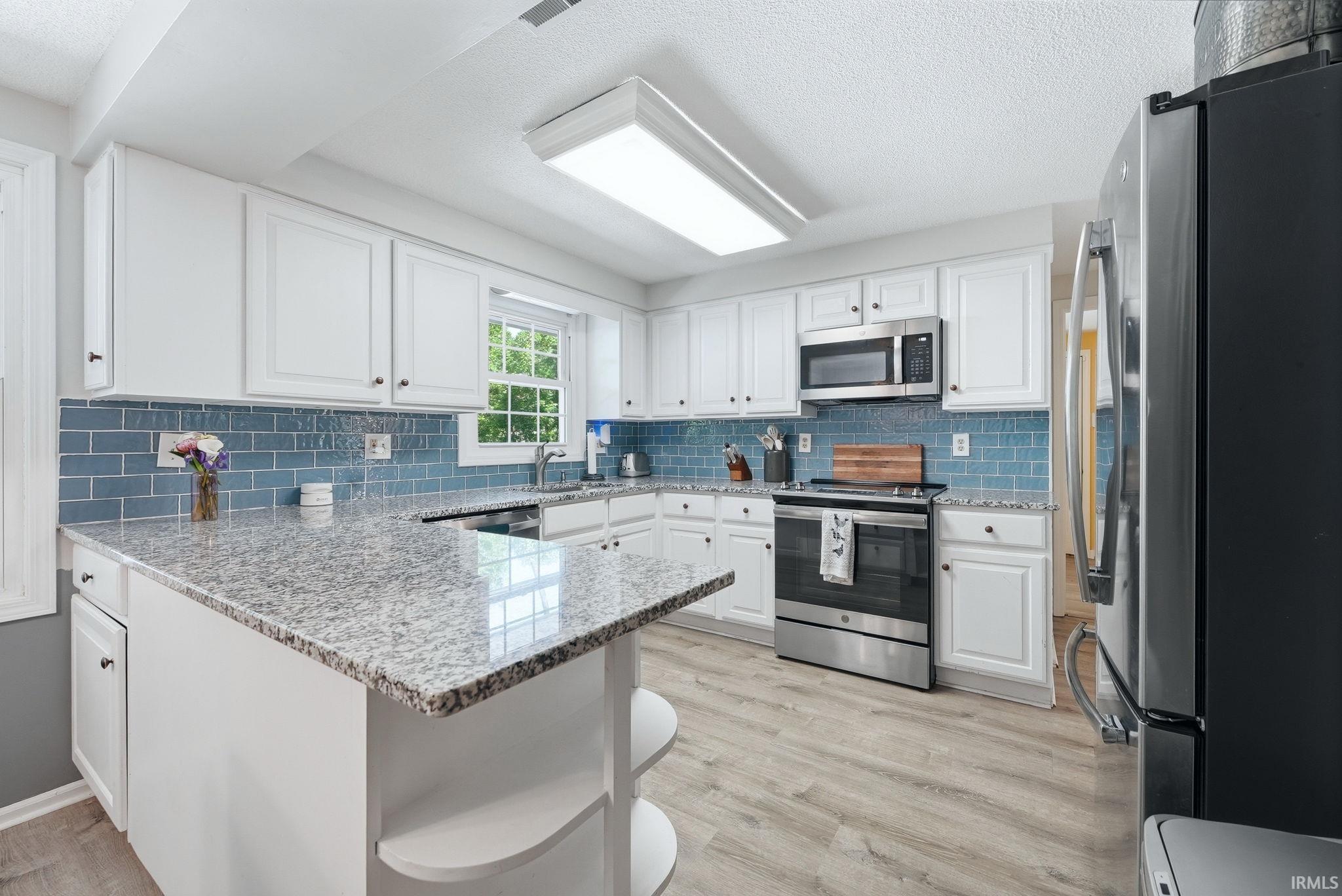Modern kitchen featuring light wood-finish flooring, white cabinetry with dark hardware, and a vibrant blue subway tile backsplash
