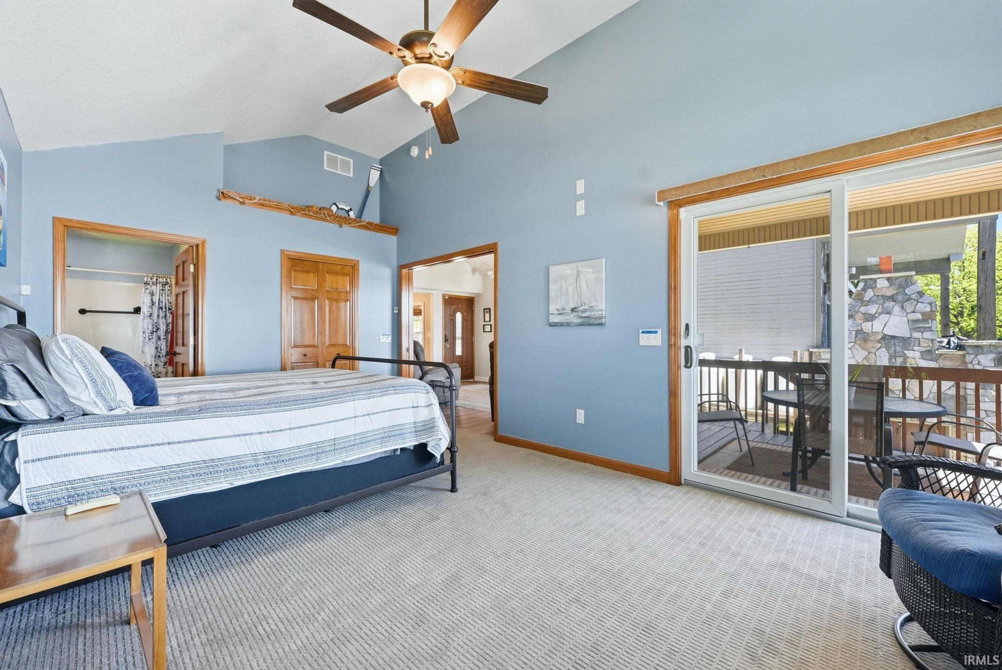 Spacious room featuring vaulted ceilings, a ceiling fan with integrated lighting, wood-finish trim, plush carpeting, and direct access to an outdoor deck through sliding glass doors