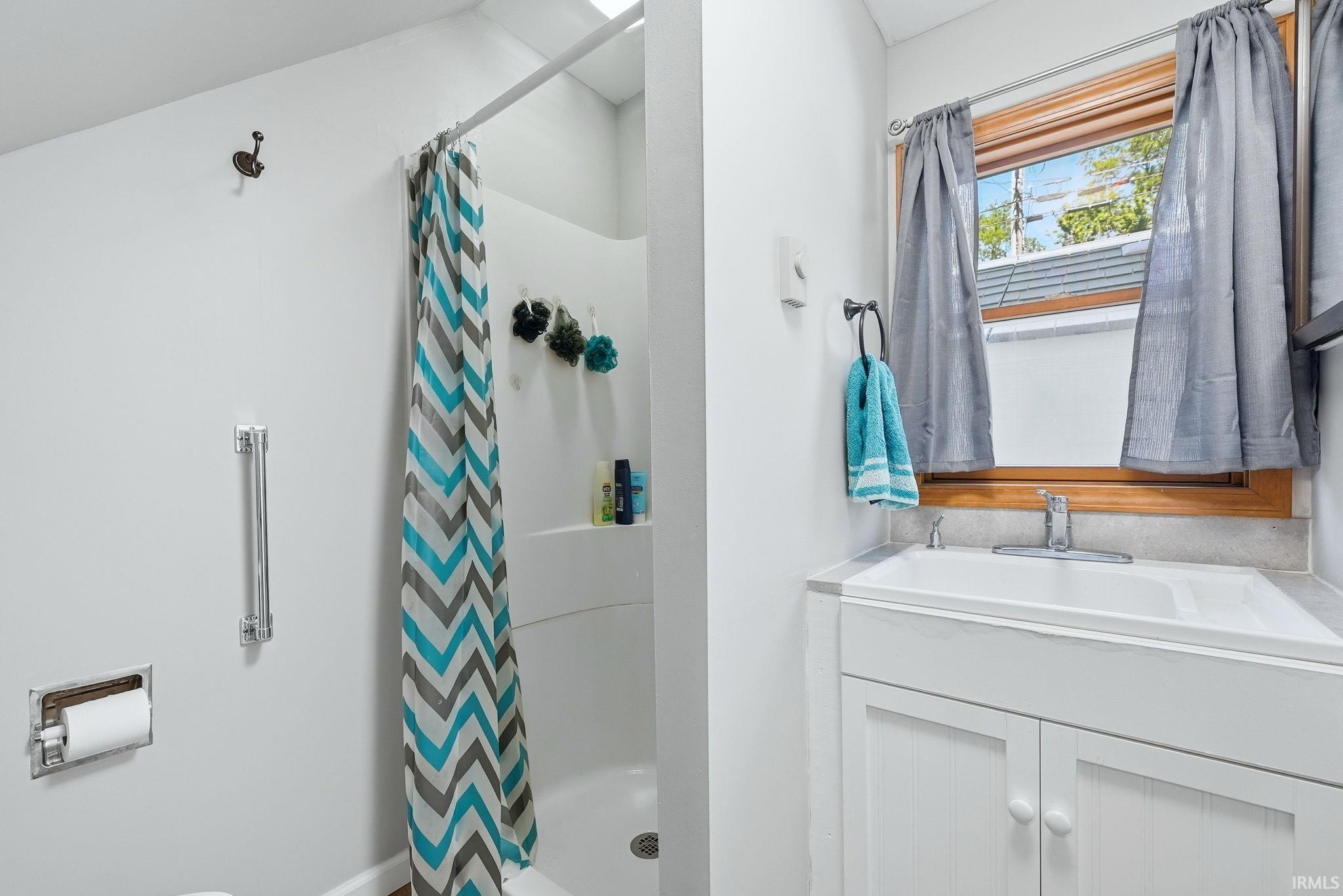 Bathroom featuring a white vanity with integrated sink, wood-framed window, and a shower with built-in shelving
