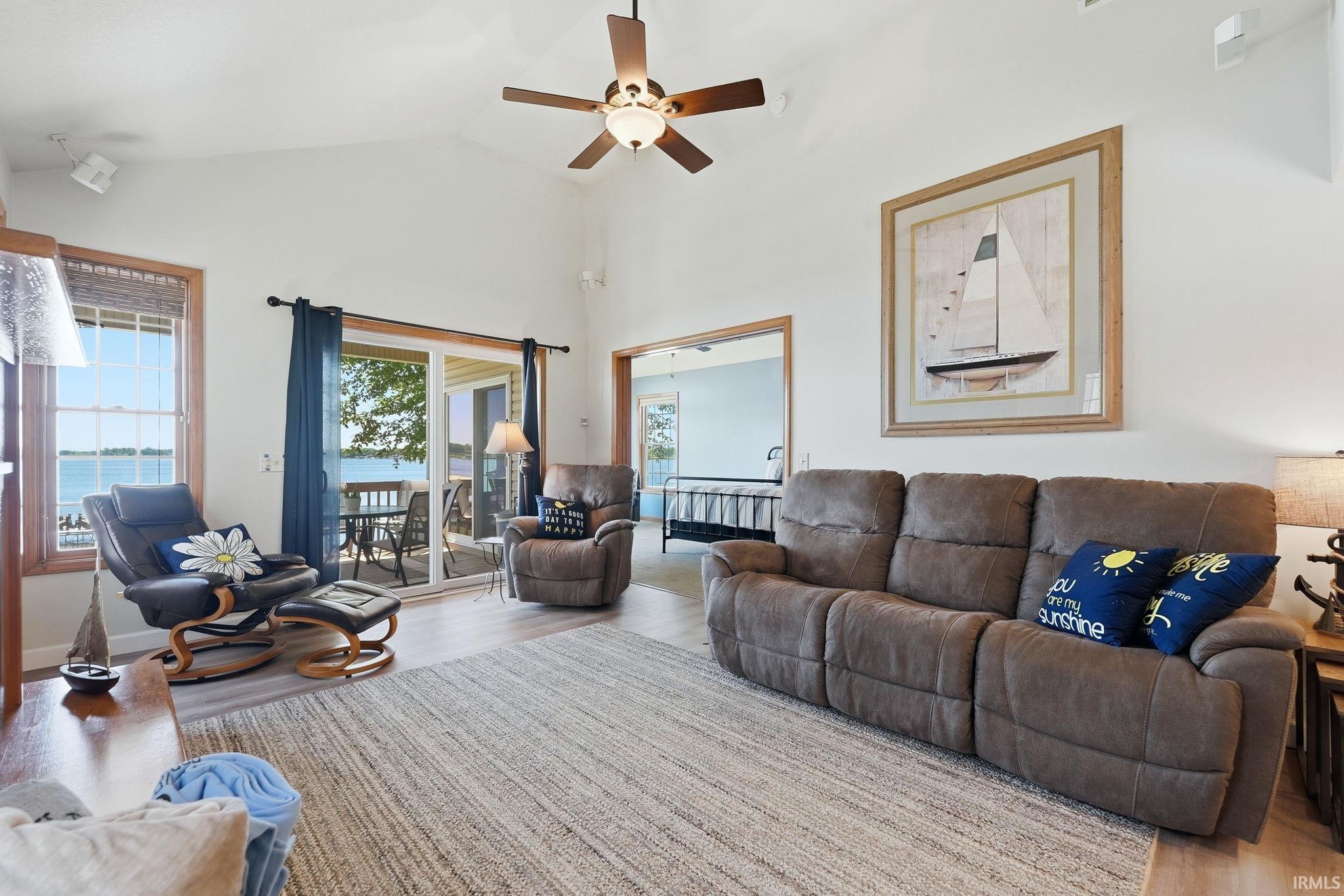 Living area featuring vaulted ceilings, wood-finish flooring, a ceiling fan with integrated lighting, and a sliding glass door opening to an exterior deck