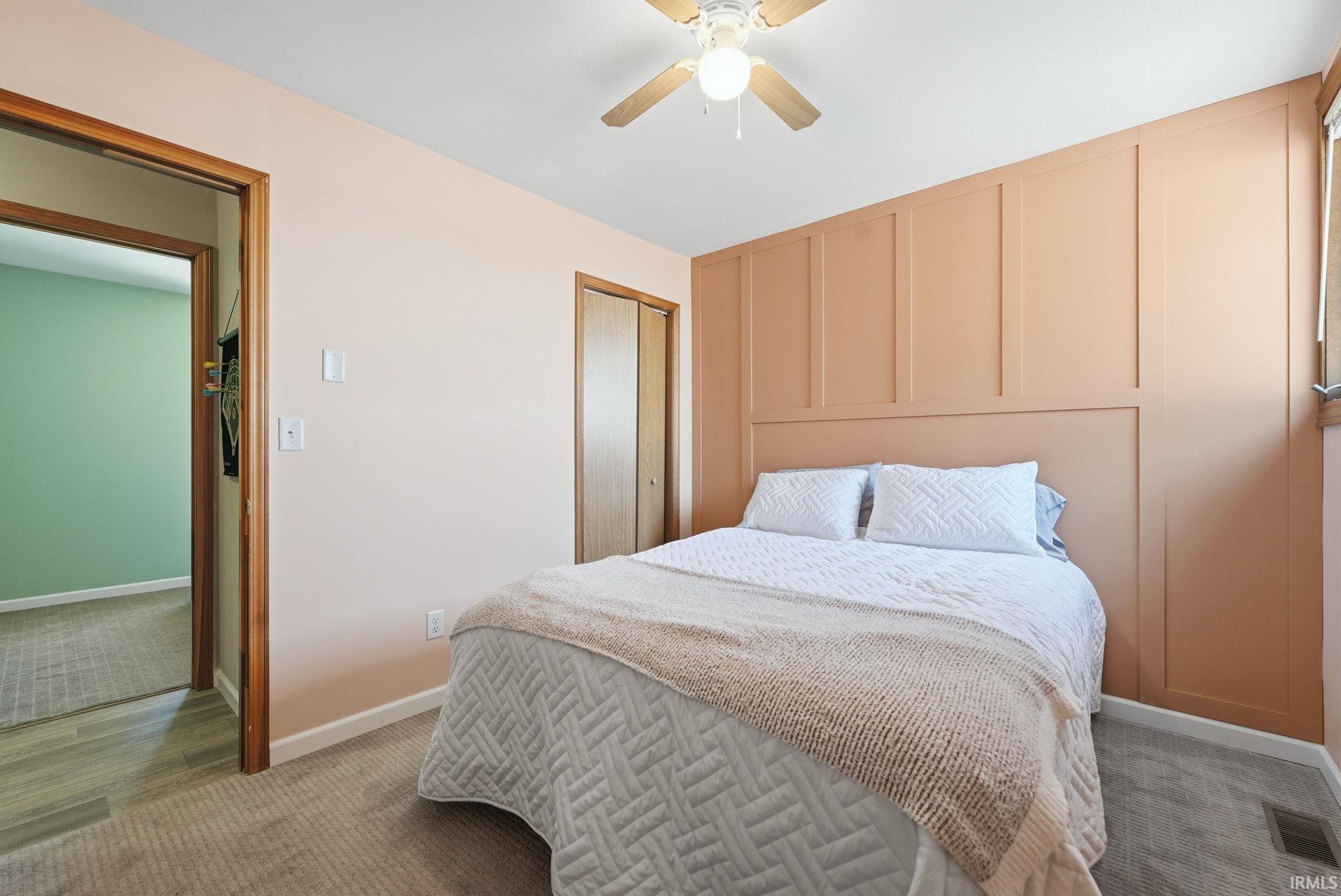 Bedroom featuring a decorative accent wall with panel molding, carpet flooring, and a ceiling fan with integrated lighting