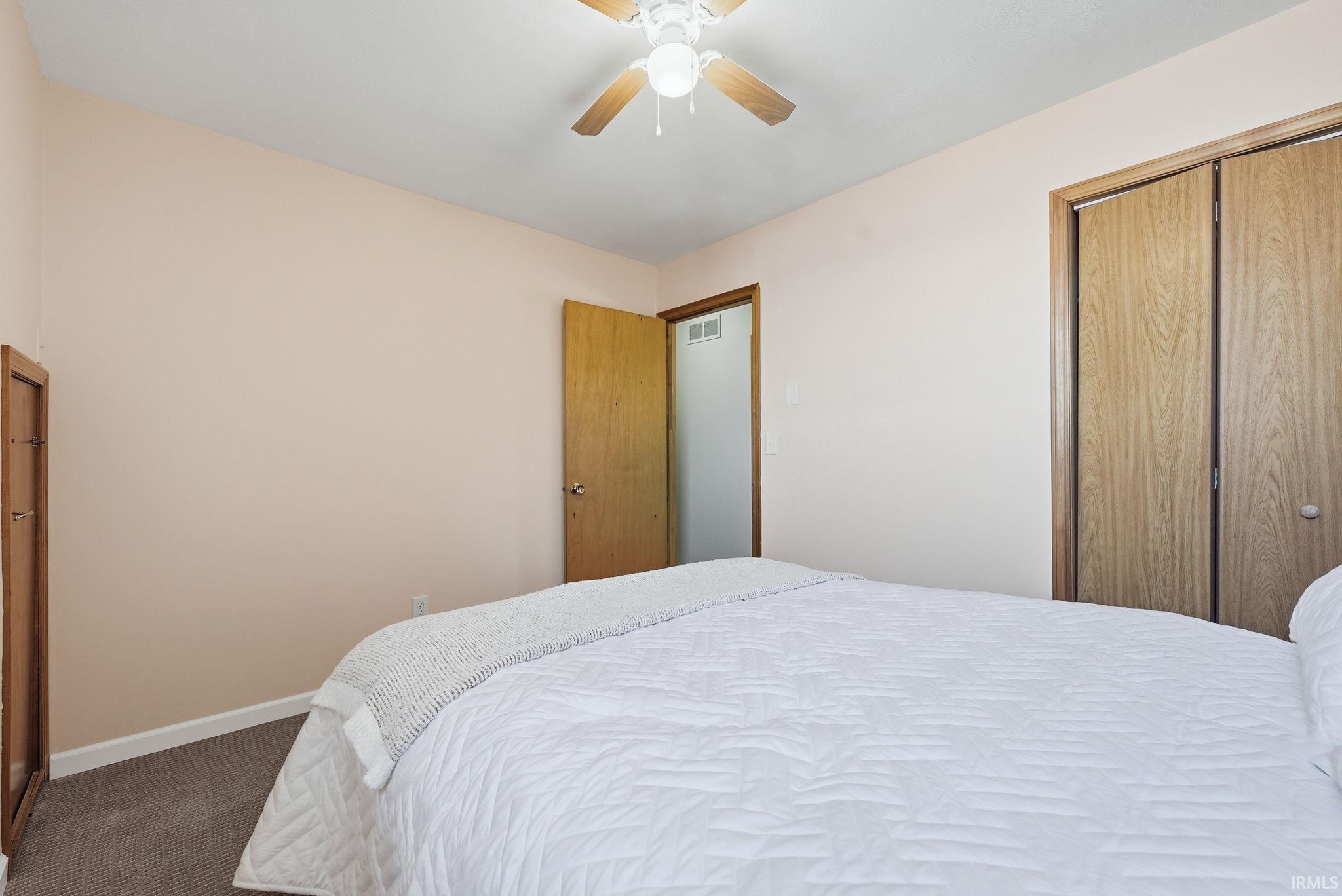 Bedroom featuring wood-finish bi-fold closet doors, a wood-finish interior door, and a ceiling fan with integrated lighting