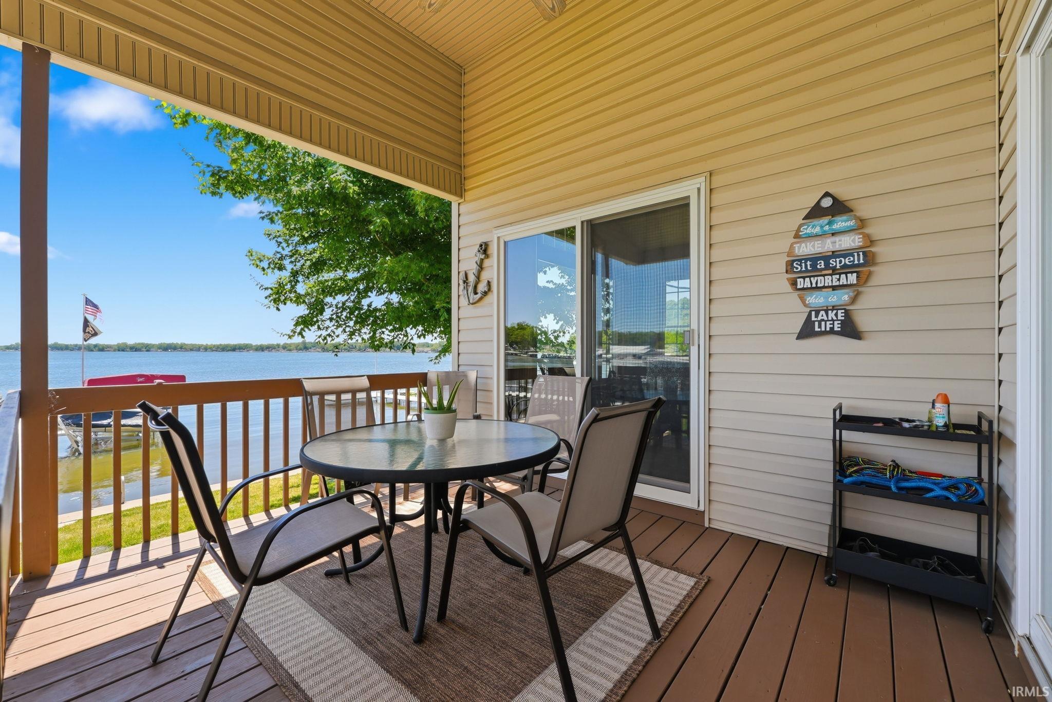 Covered outdoor deck with water frontage, featuring composite decking, wooden railings, and a sliding glass door