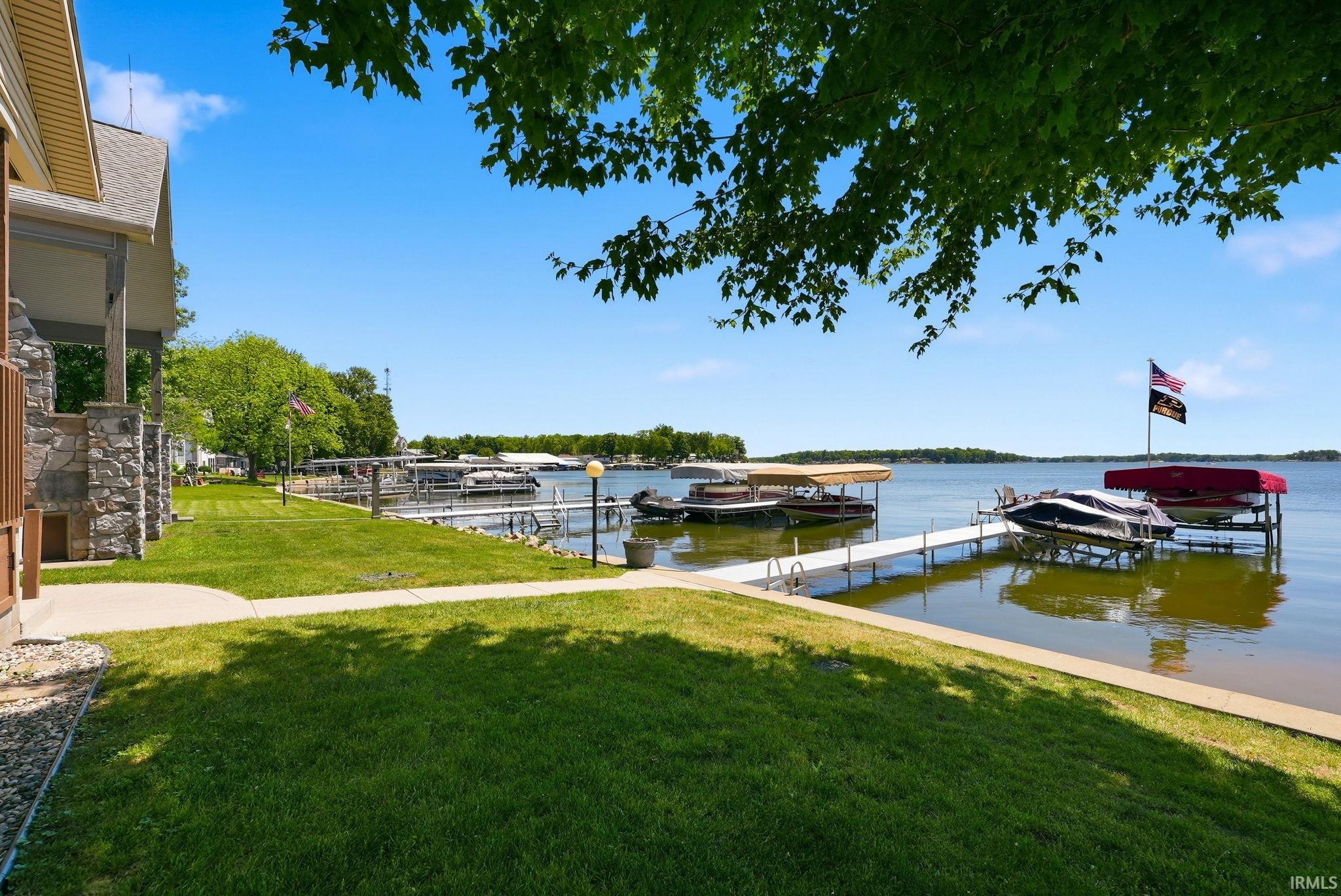 Waterfront property featuring a private dock system, direct lake access, a stone-clad exterior, and a manicured lawn