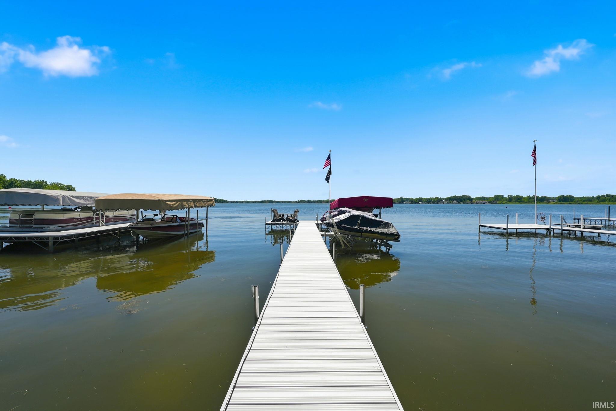 Expansive waterfront setting featuring a lengthy dock extending into the water, multiple boat slips with canopies, and additional docking structures