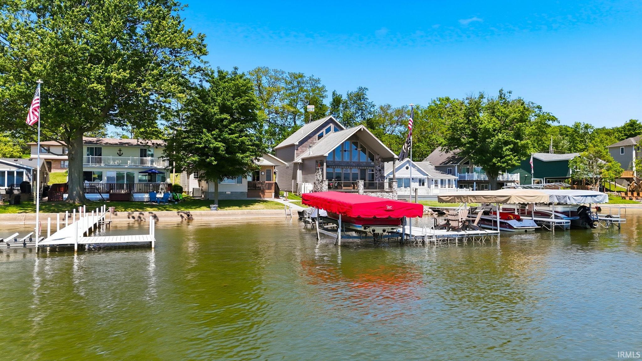 Waterfront property featuring a private dock, boat lift with red canopy, sandy shoreline, and mature trees