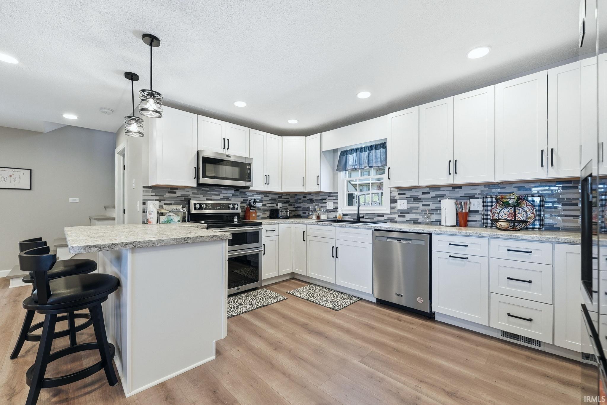 Contemporary kitchen featuring white cabinetry, stainless steel appliances, wood-finish flooring, recessed lighting, and a breakfast bar with pendant lights