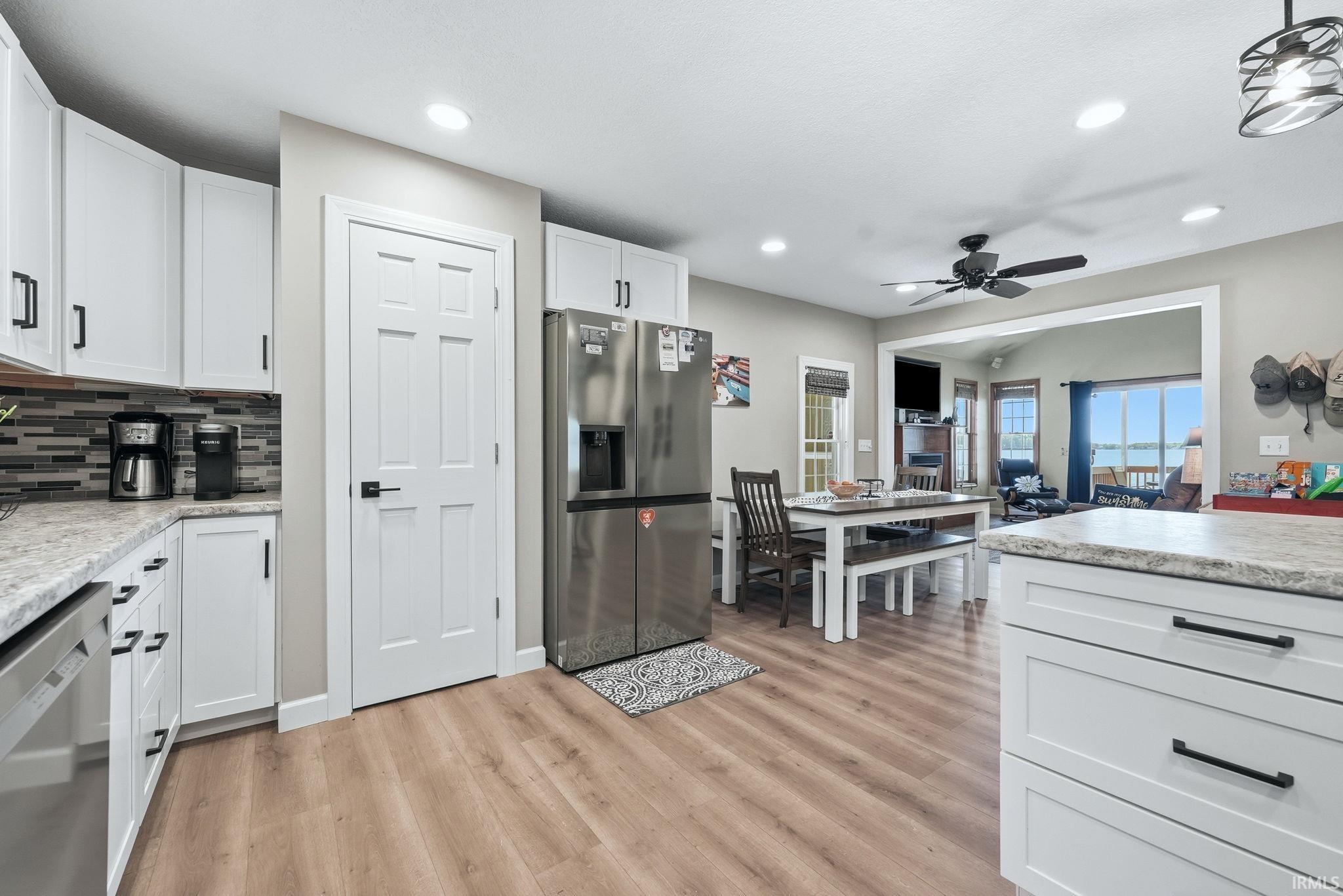 Modern kitchen featuring white cabinetry with matte black hardware, light wood-finish flooring, recessed lighting, and a stainless steel refrigerator