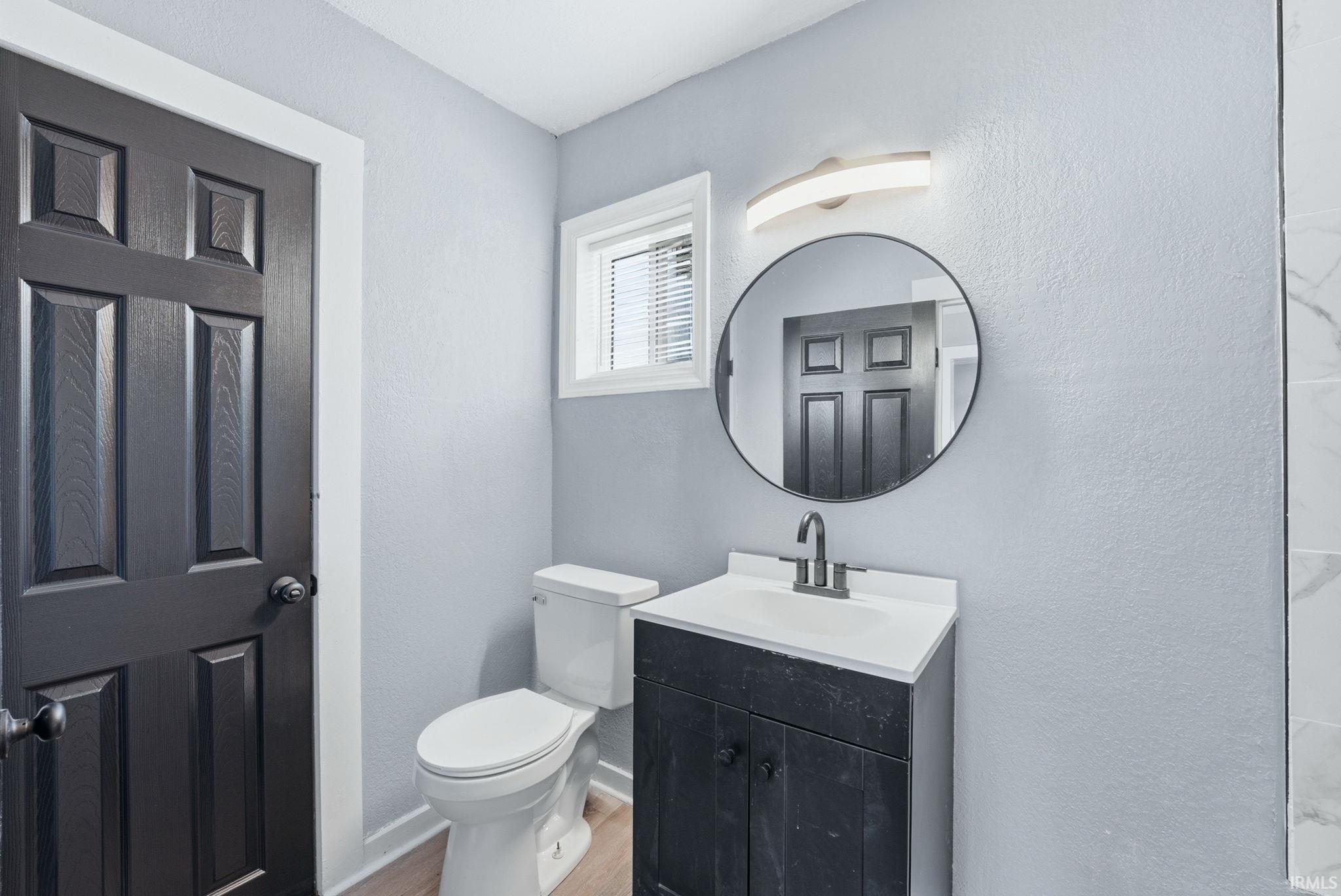 Bathroom featuring a dark wood-finish vanity with a white countertop, a circular mirror, and a modern light fixture