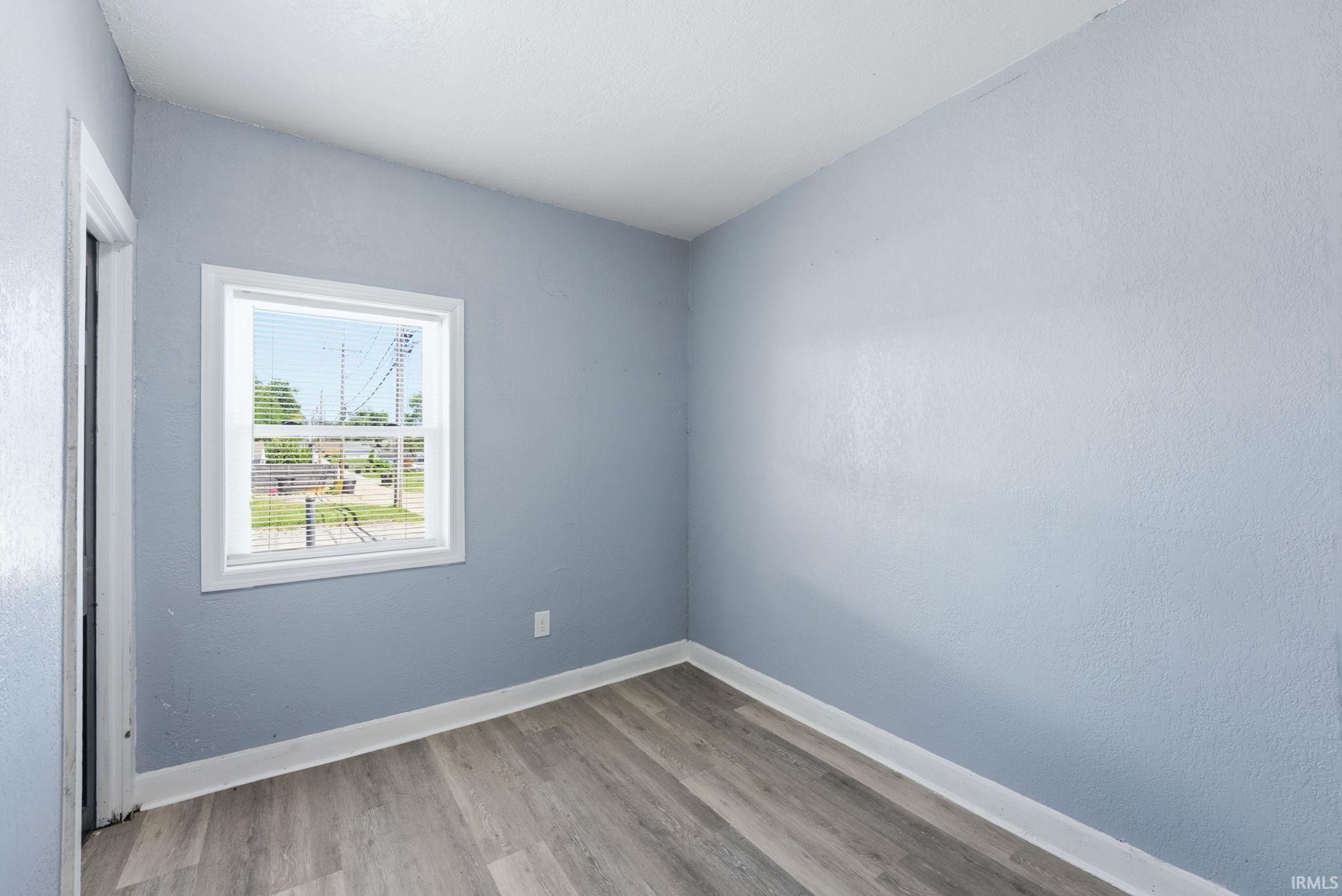 Room featuring wood-finish flooring, light blue wall paint, white baseboards, and a white-framed window with horizontal blinds