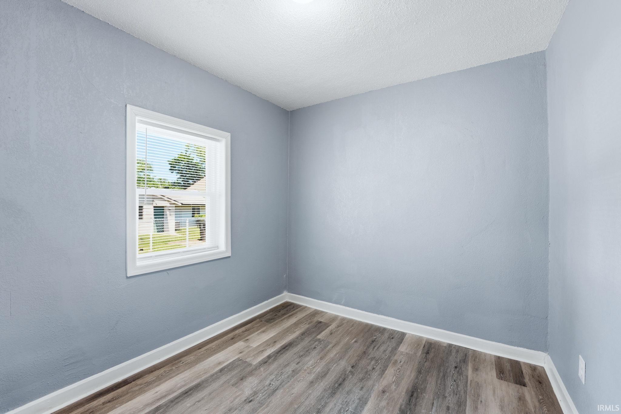 Bright room featuring a single window with blinds, light blue wall paint, wood-finish flooring, white baseboards, and a white ceiling