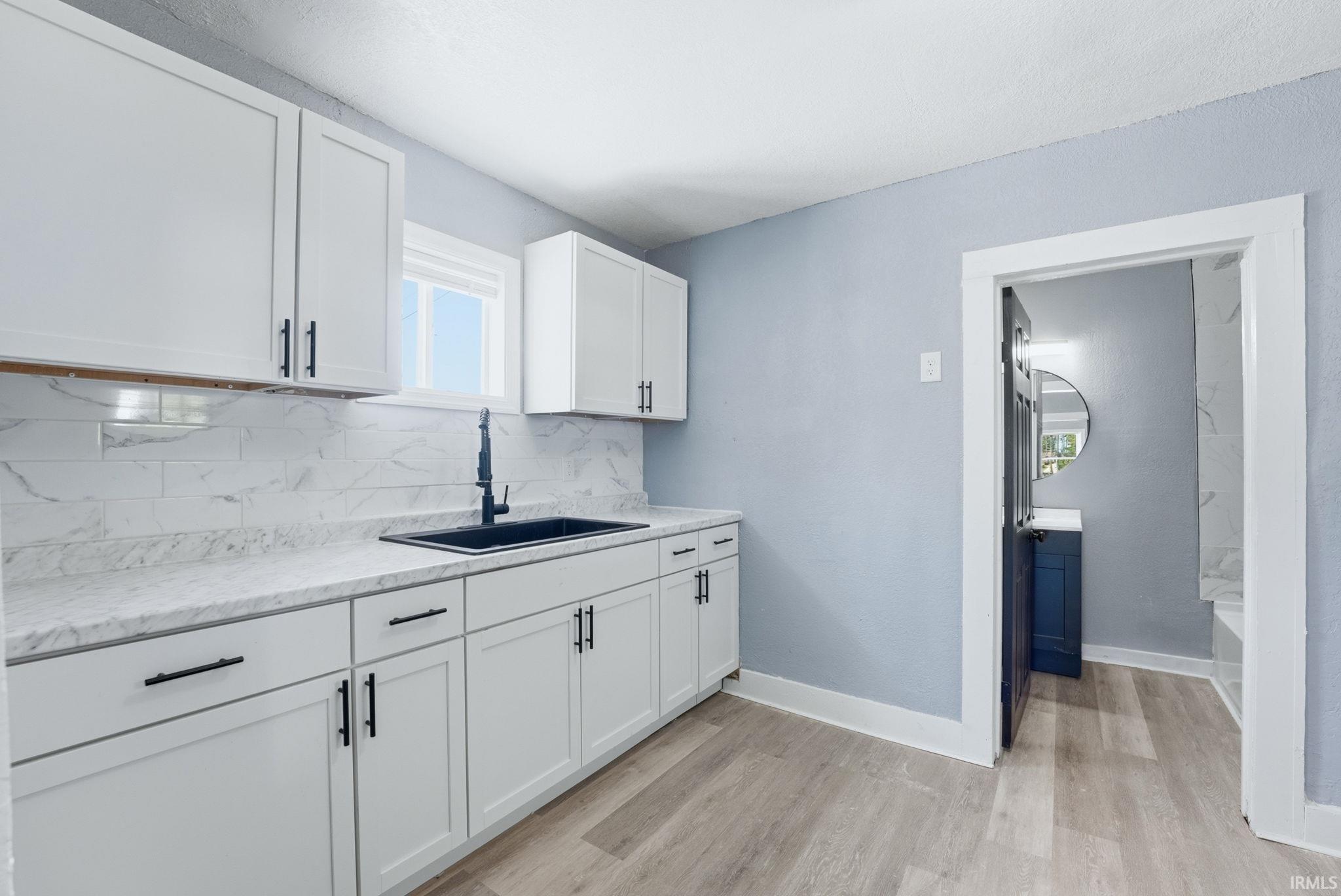 Kitchen featuring white shaker-style cabinetry with matte black hardware, white stone-finish countertops, and a subway tile backsplash