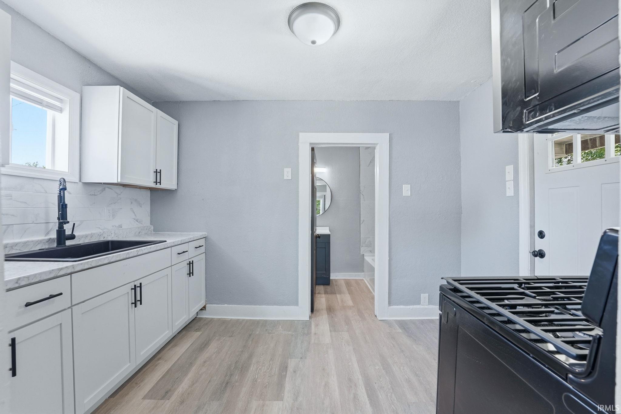 Kitchen featuring white shaker cabinetry with matte black hardware, light-toned wood-finish flooring, and a black range