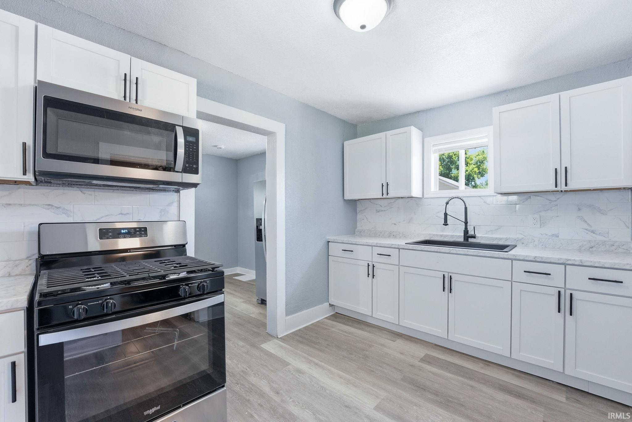 Modern kitchen featuring white shaker cabinetry with black hardware, stainless steel appliances, light-colored countertops, and a subway tile backsplash