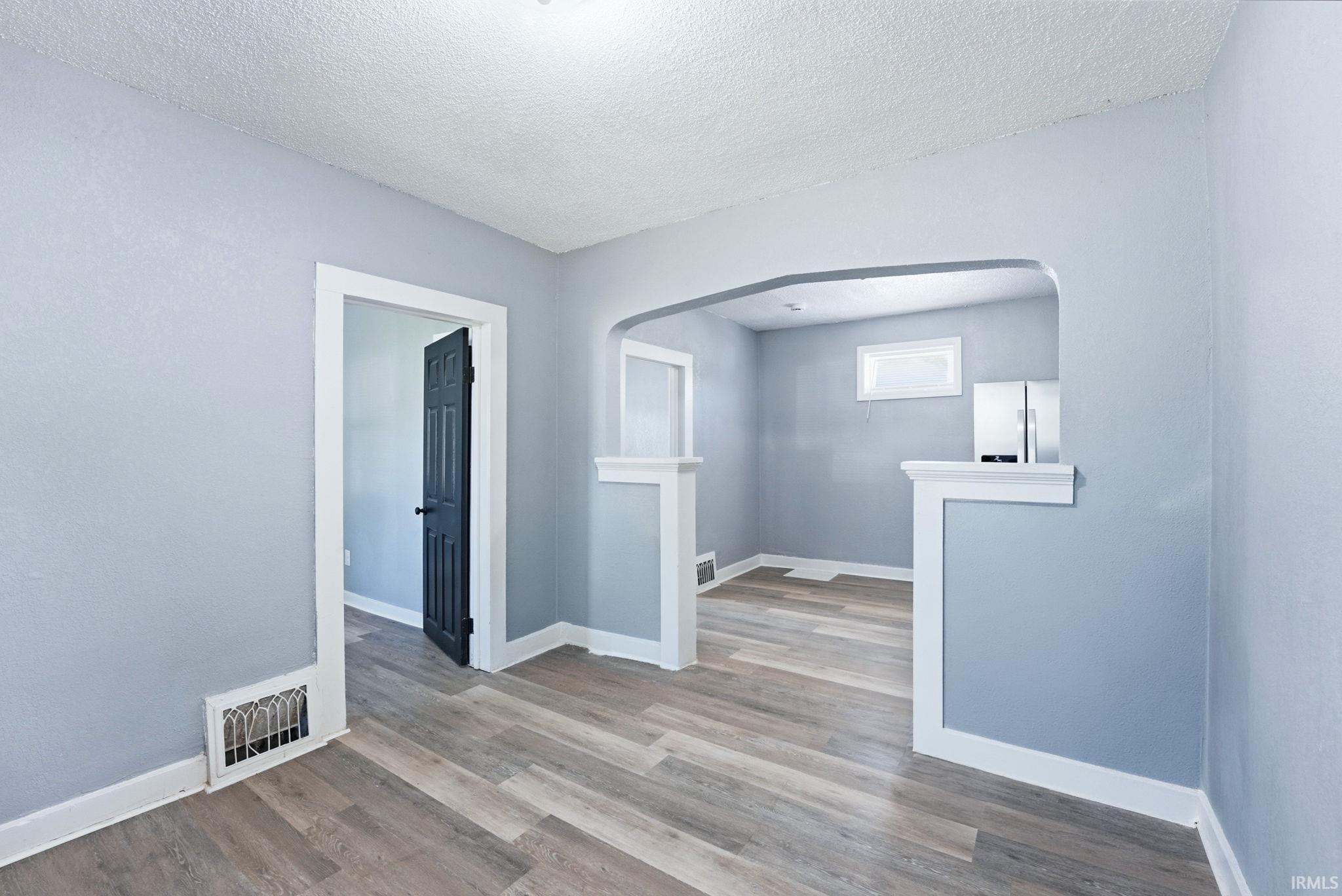 Open concept room featuring wood-finish flooring, light grey wall paint, white trim, and a built-in archway