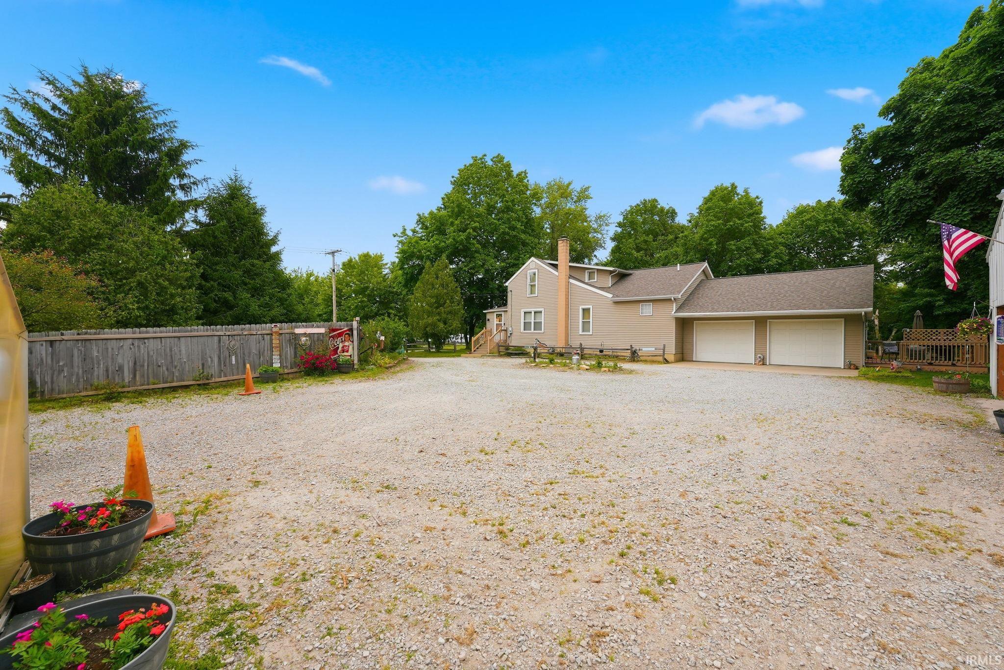 Gravel driveway offering extensive parking, two-car garage, and a privacy fence