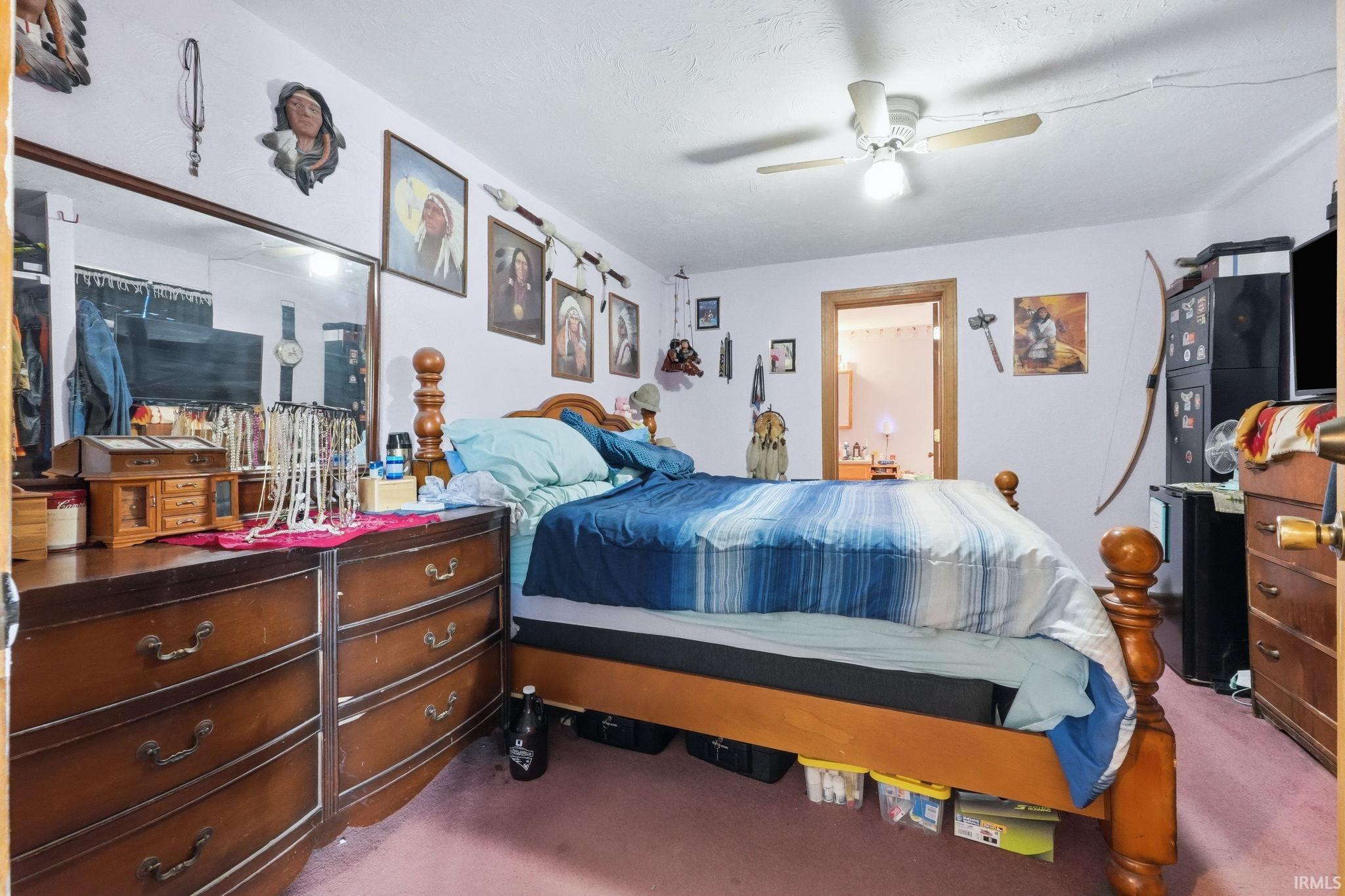 Carpeted room featuring a ceiling fan with integrated lighting, a wooden bed frame, and a doorway leading to an interior space
