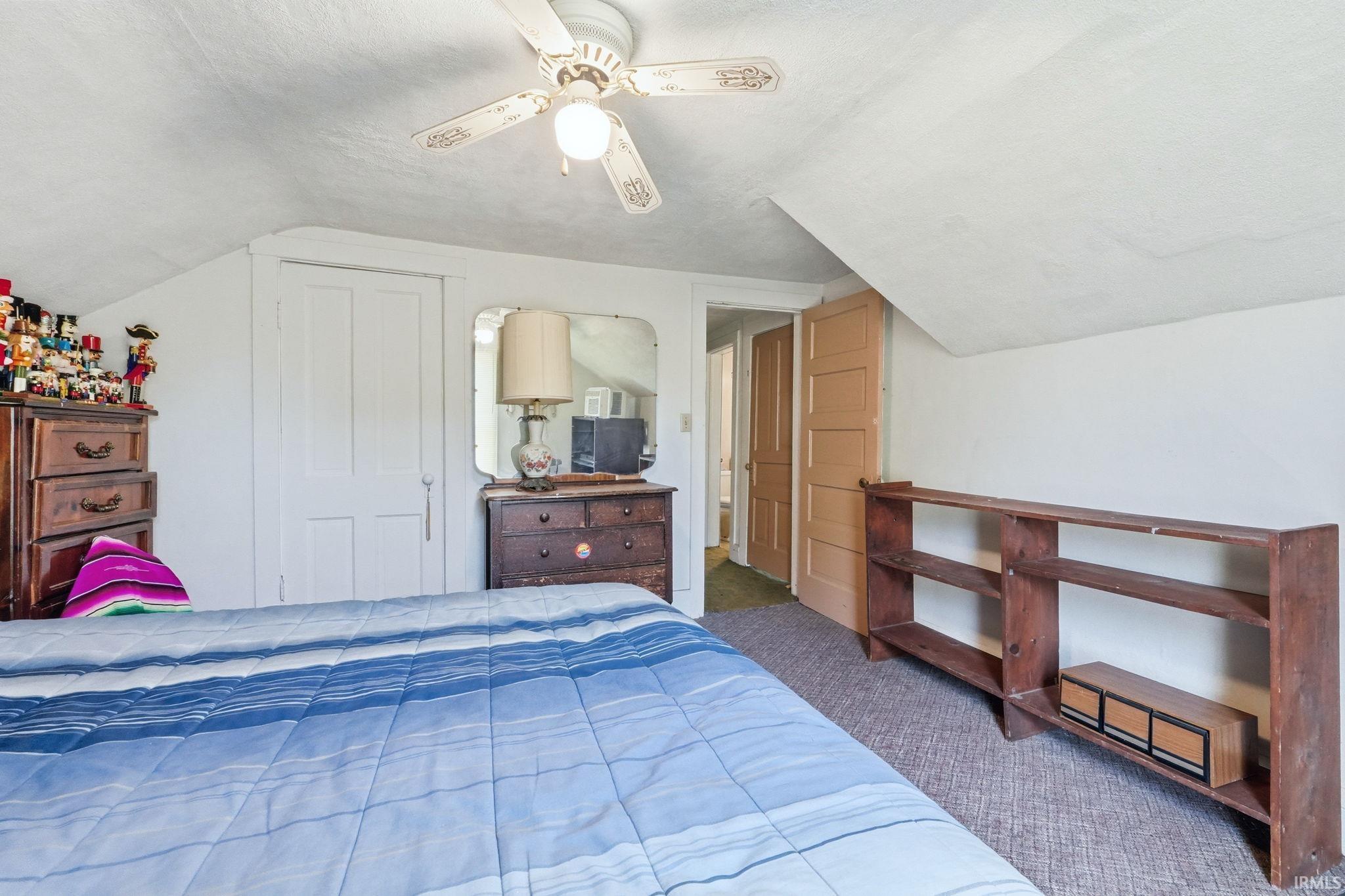 Bedroom featuring a ceiling fan, white paneled door, and sloped ceiling