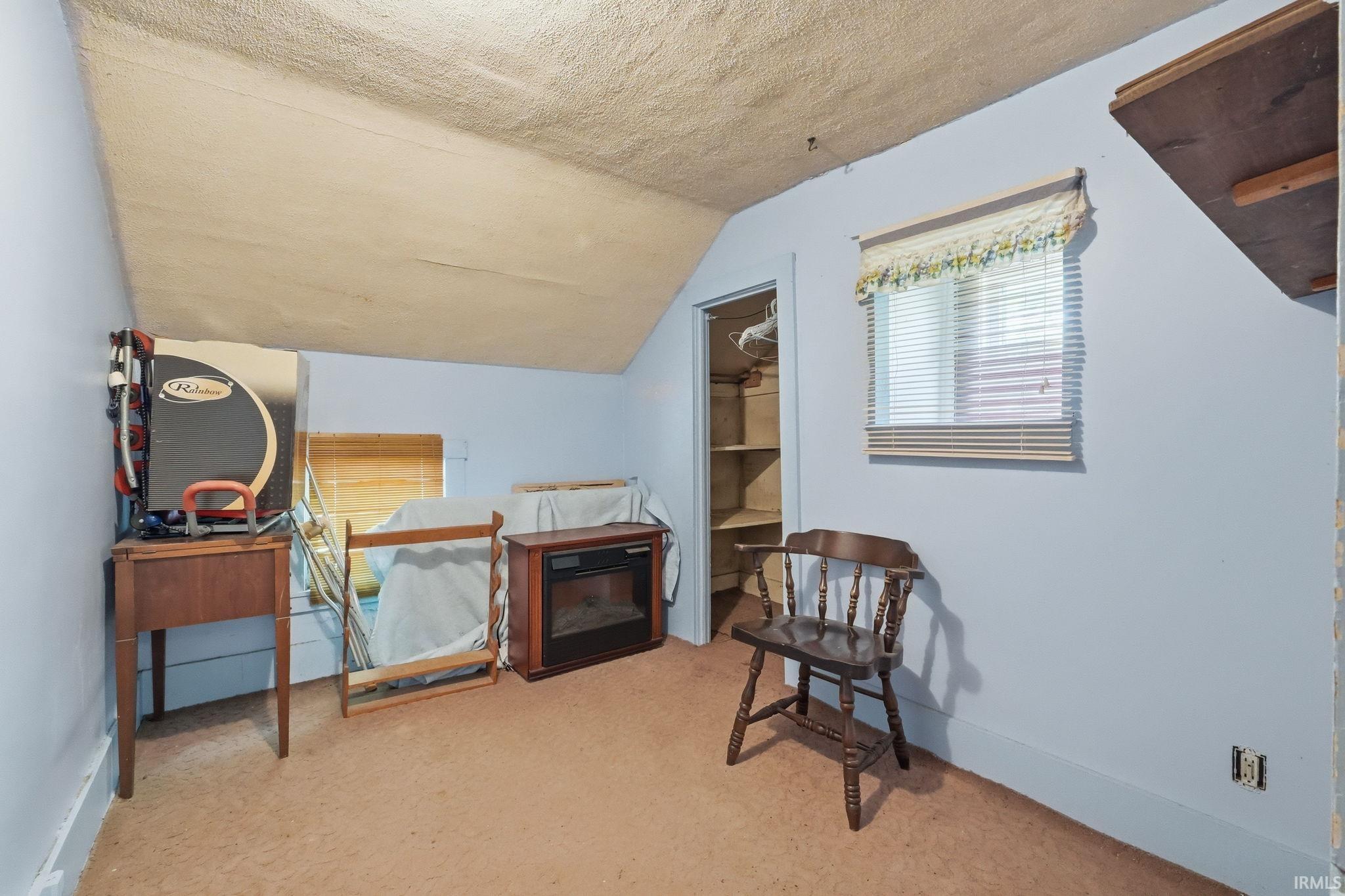 Sloped ceiling room featuring a window with blinds, light blue walls, and a recessed open closet with shelving